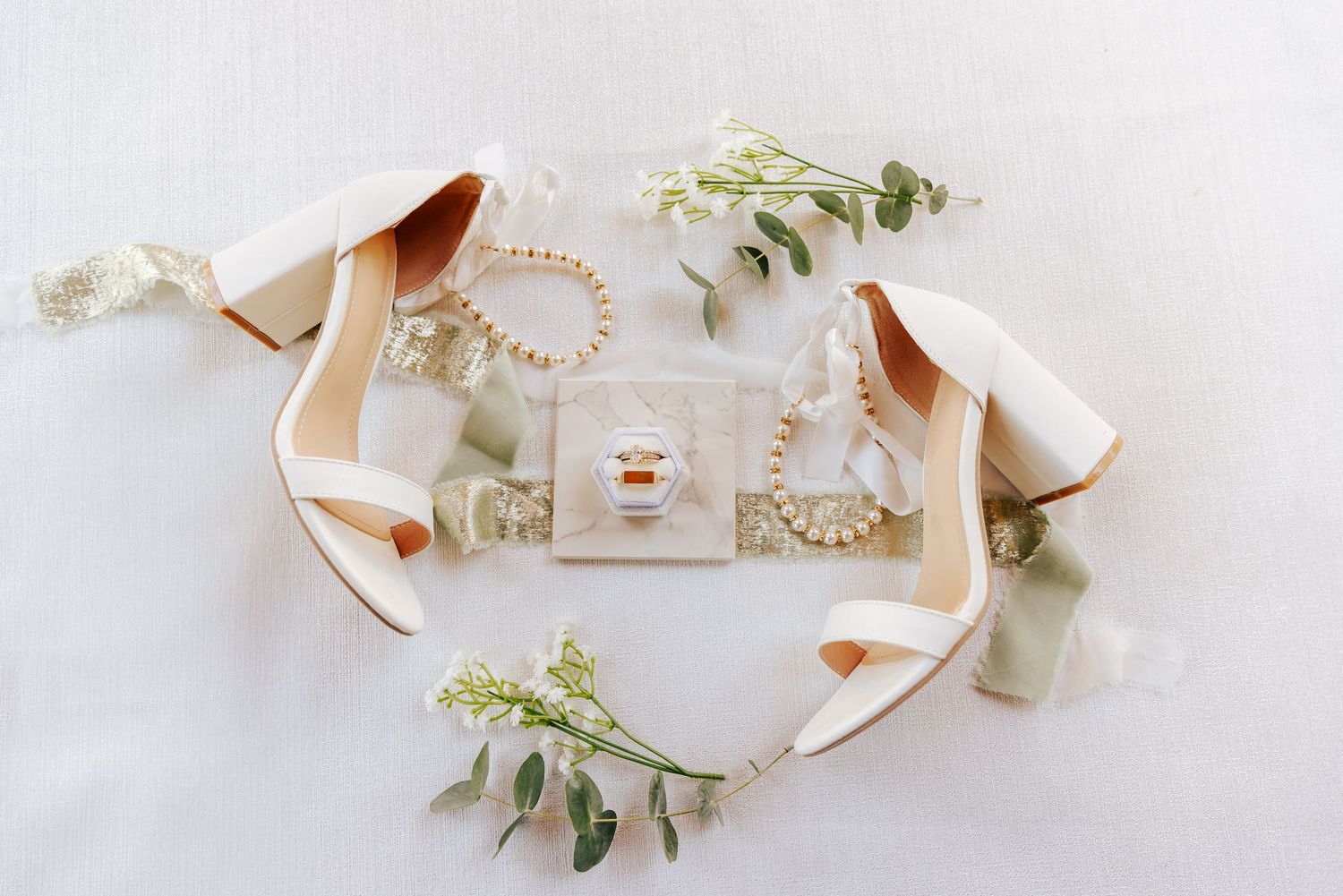Wedding details flatlay with vintage black and white photo, pearl necklace, perfume bottle, white shoes and daisies.