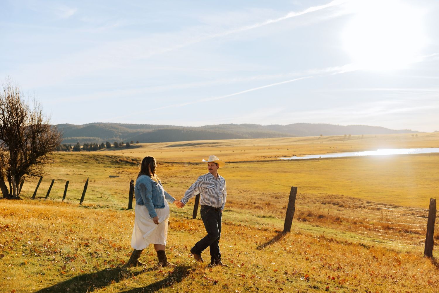 A couple walks hand in hand through golden field at sunset.