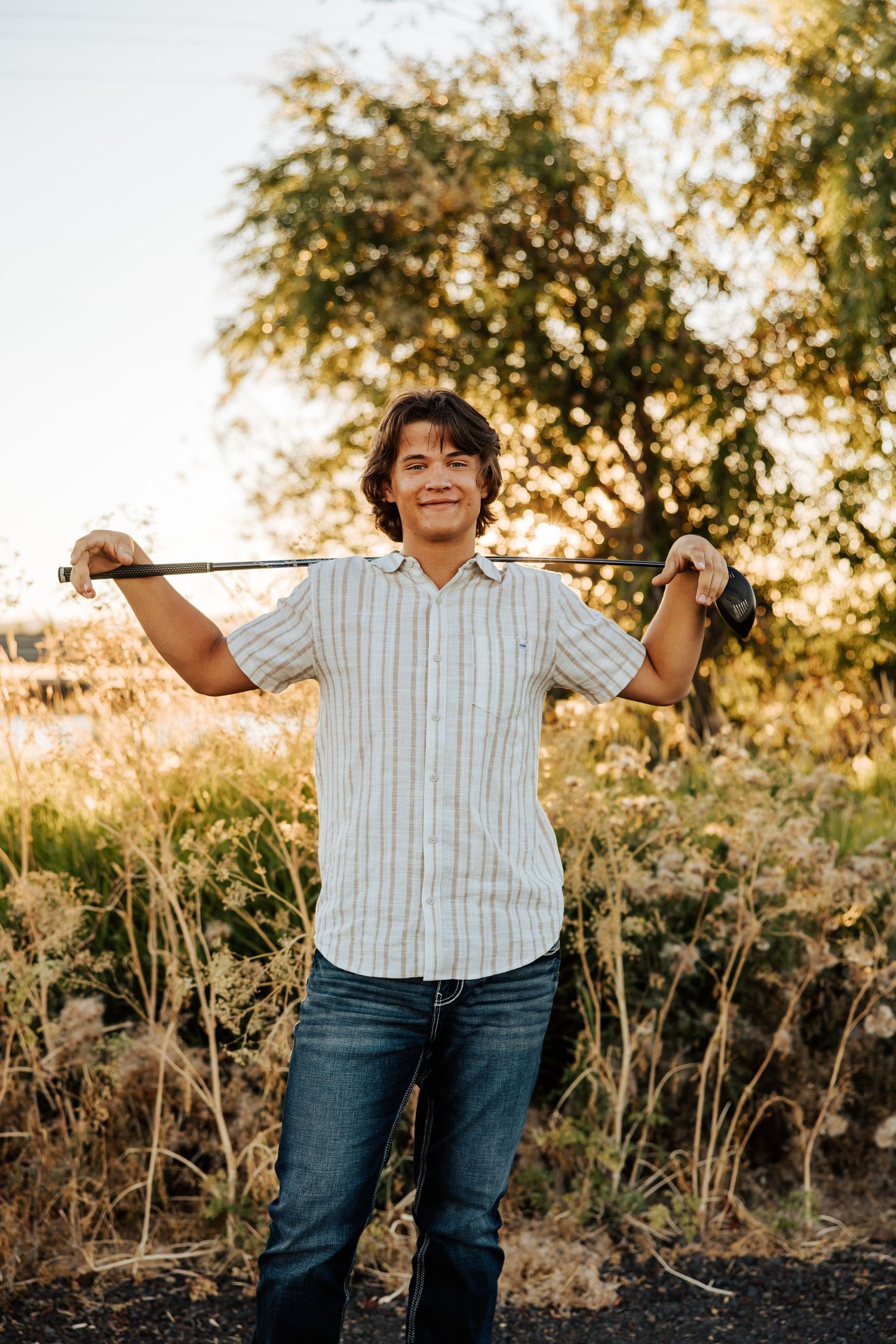 A casual outdoor photo shoot featuring jeans and a striped shirt against a golden hour backdrop.
