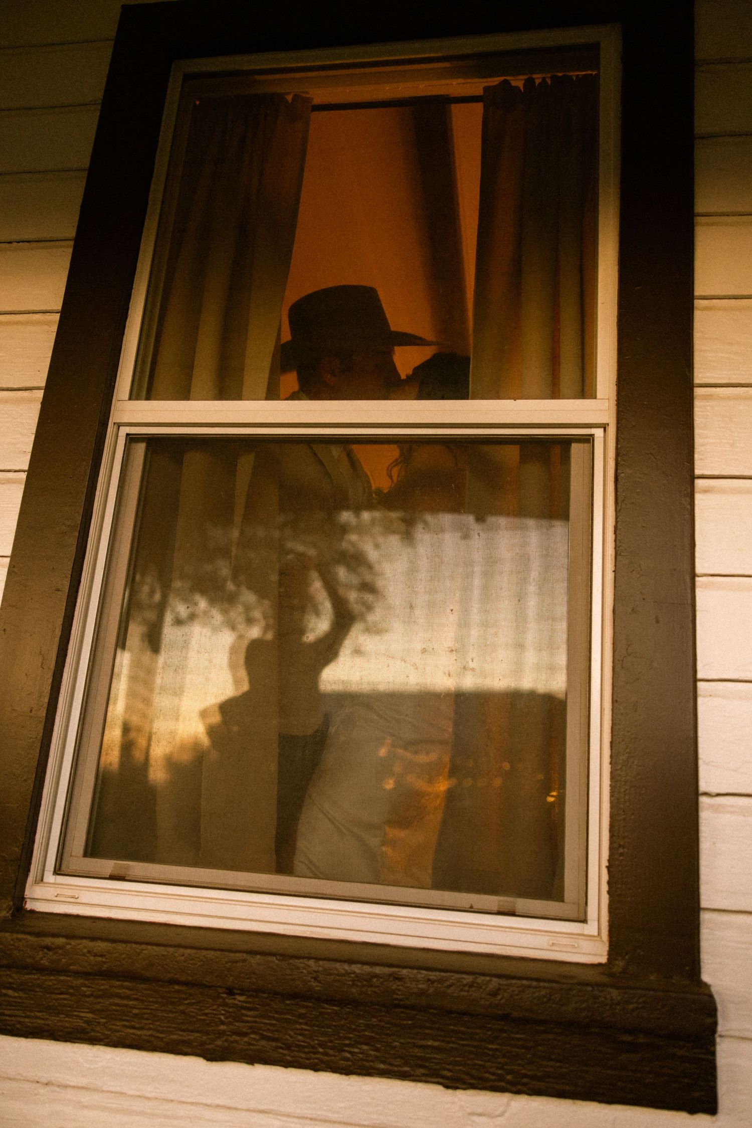 Silhouetted figures visible through a window frame at sunset creating a romantic atmosphere.