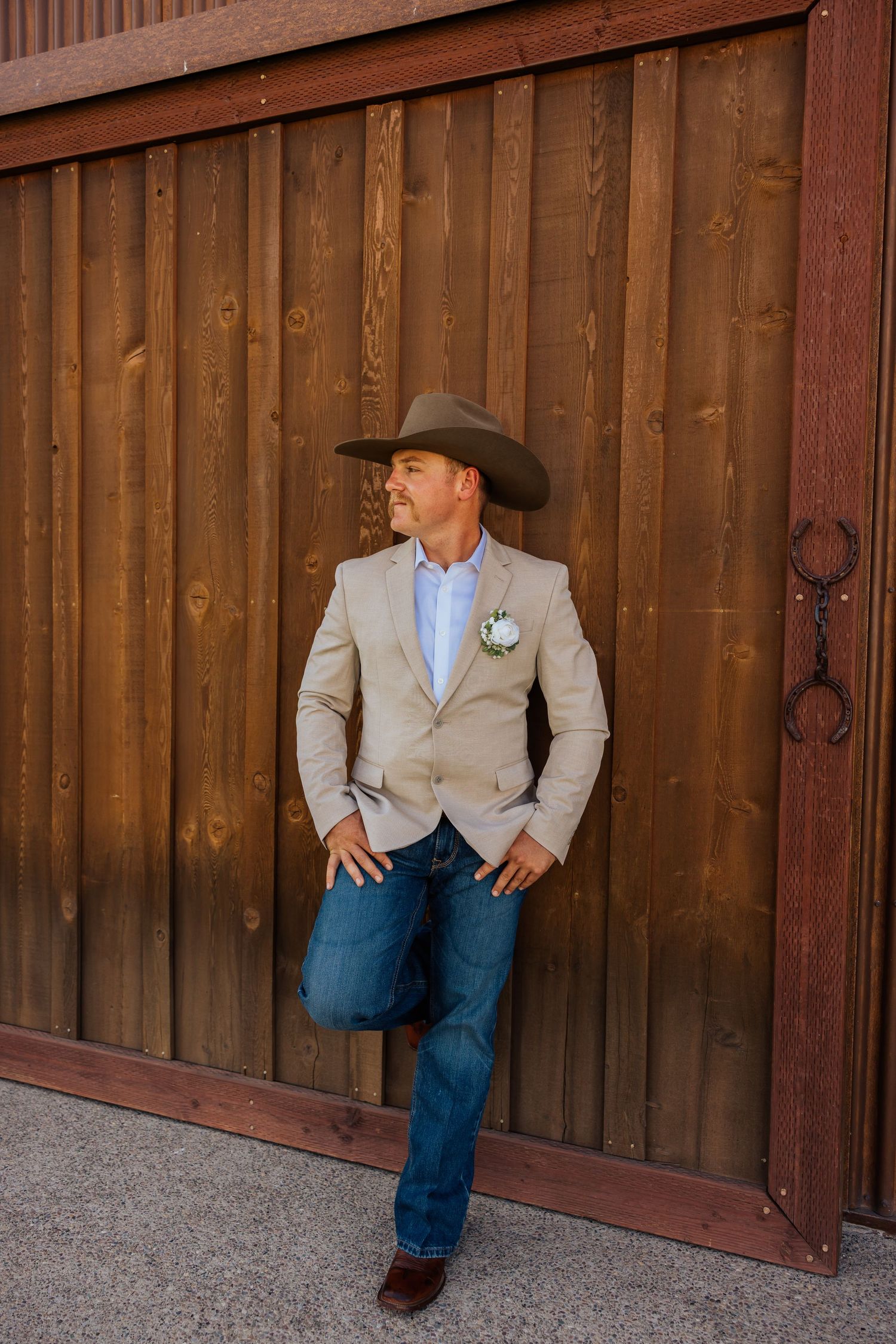 Groom in a beige suit jacket and jeans poses against a rustic wooden wall in three candid shots.