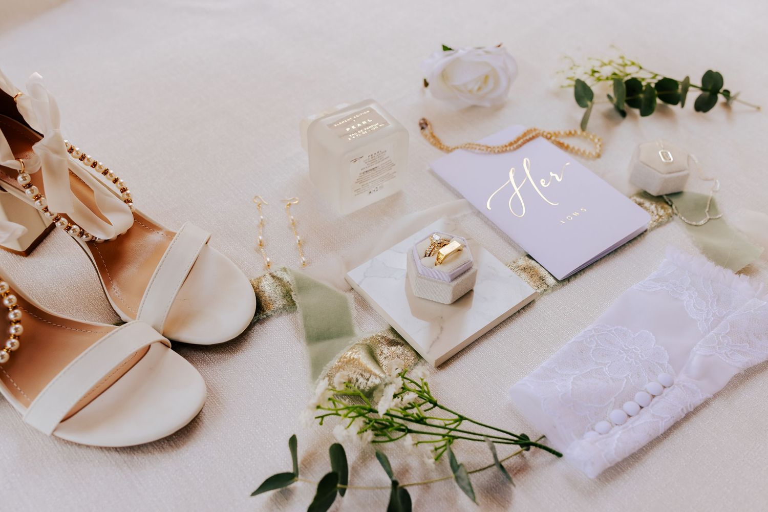 Minimalist wedding flat lay with white shoes, stationery and floral accents.