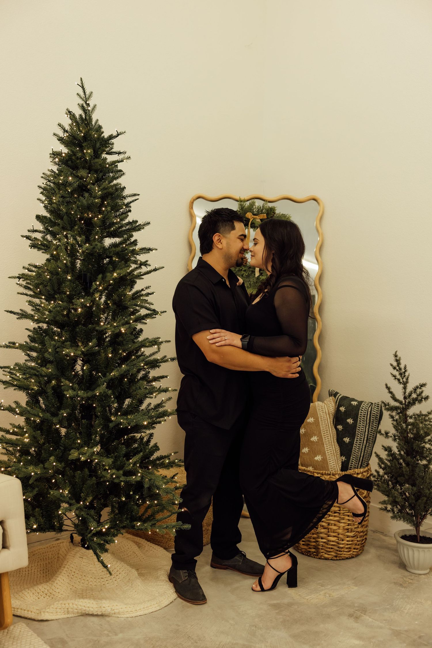 Romantic couple embracing by a decorated Christmas tree in a cozy living room setting.