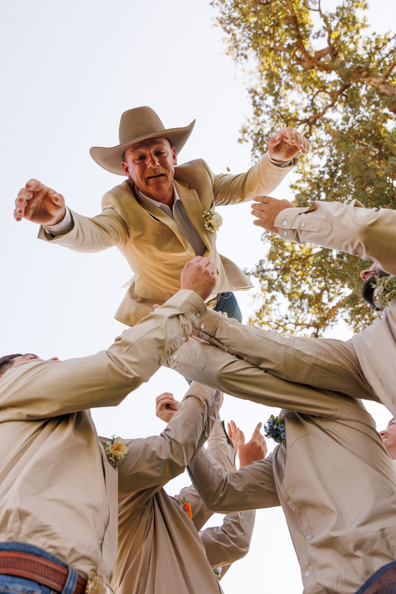 A dynamic low-angle shot of groomsmen lifting someone in celebration against a bright sky.