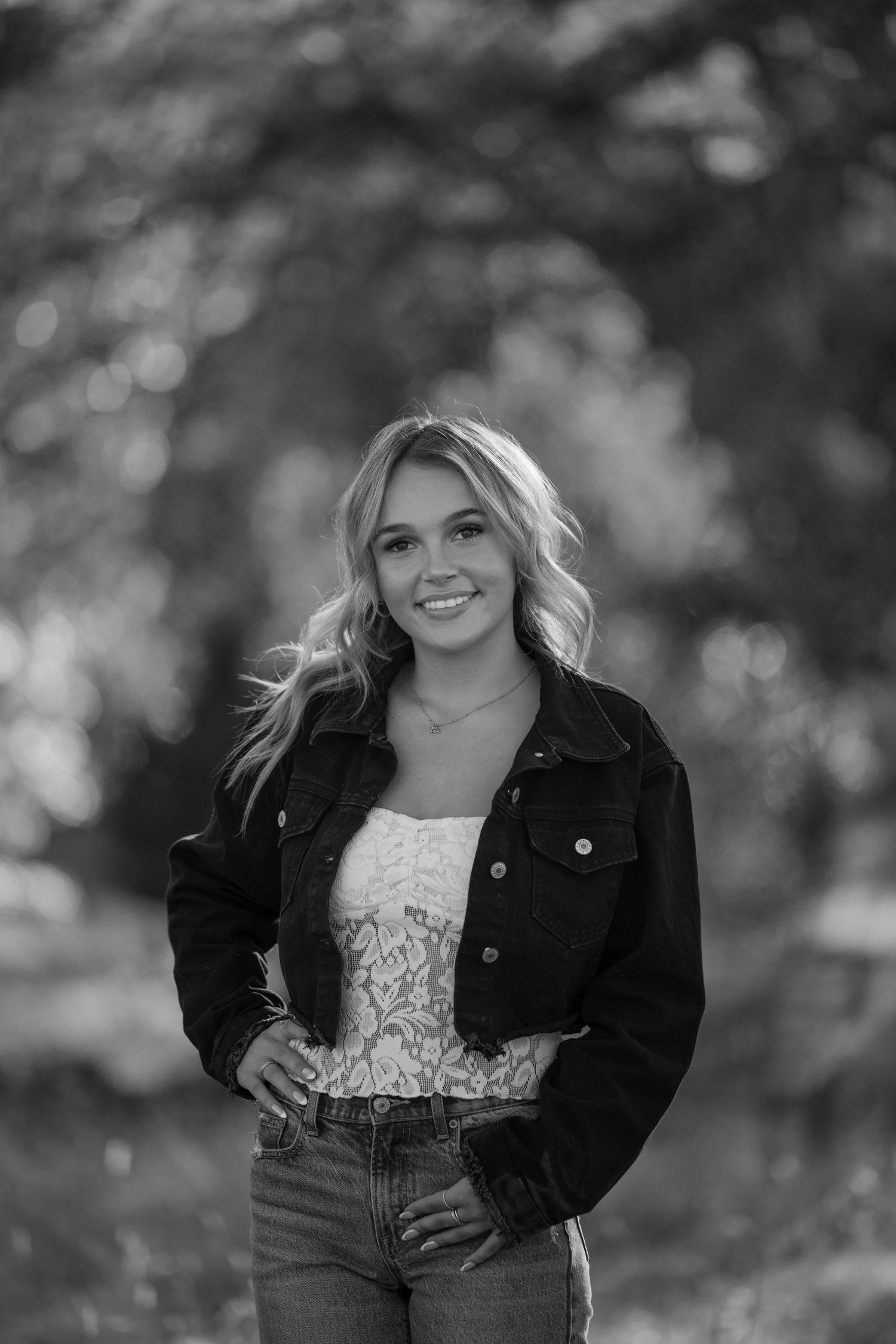 Portrait against blurred nature backdrop wearing denim jacket and lace top in monochrome.