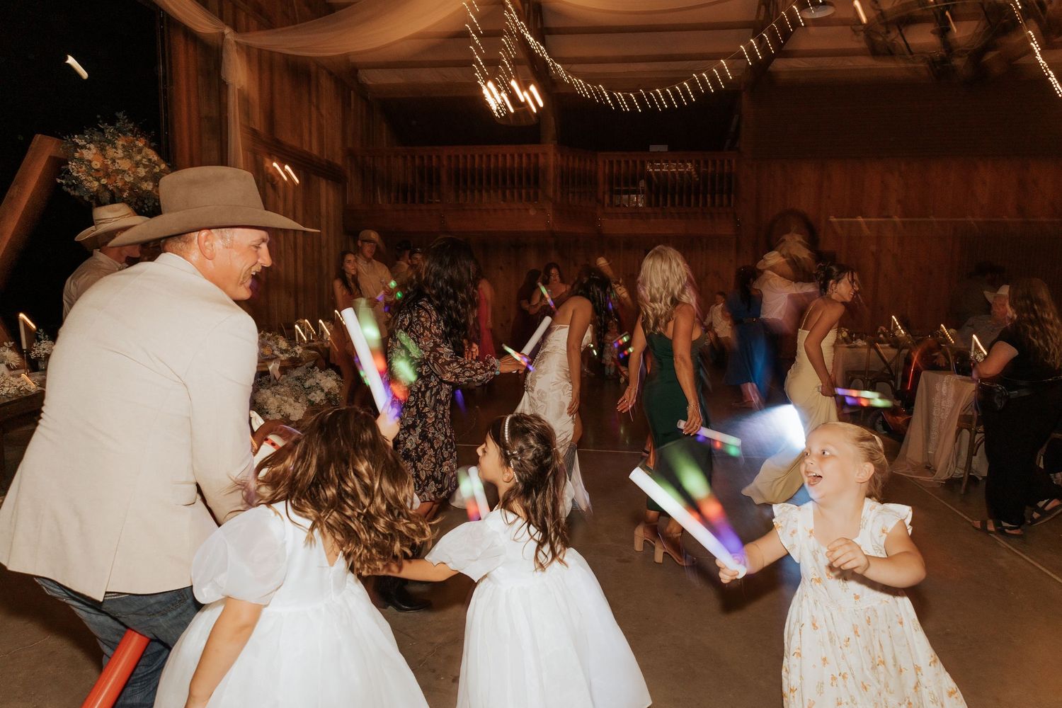 Lively dance floor scene at country wedding with glow sticks and celebration.