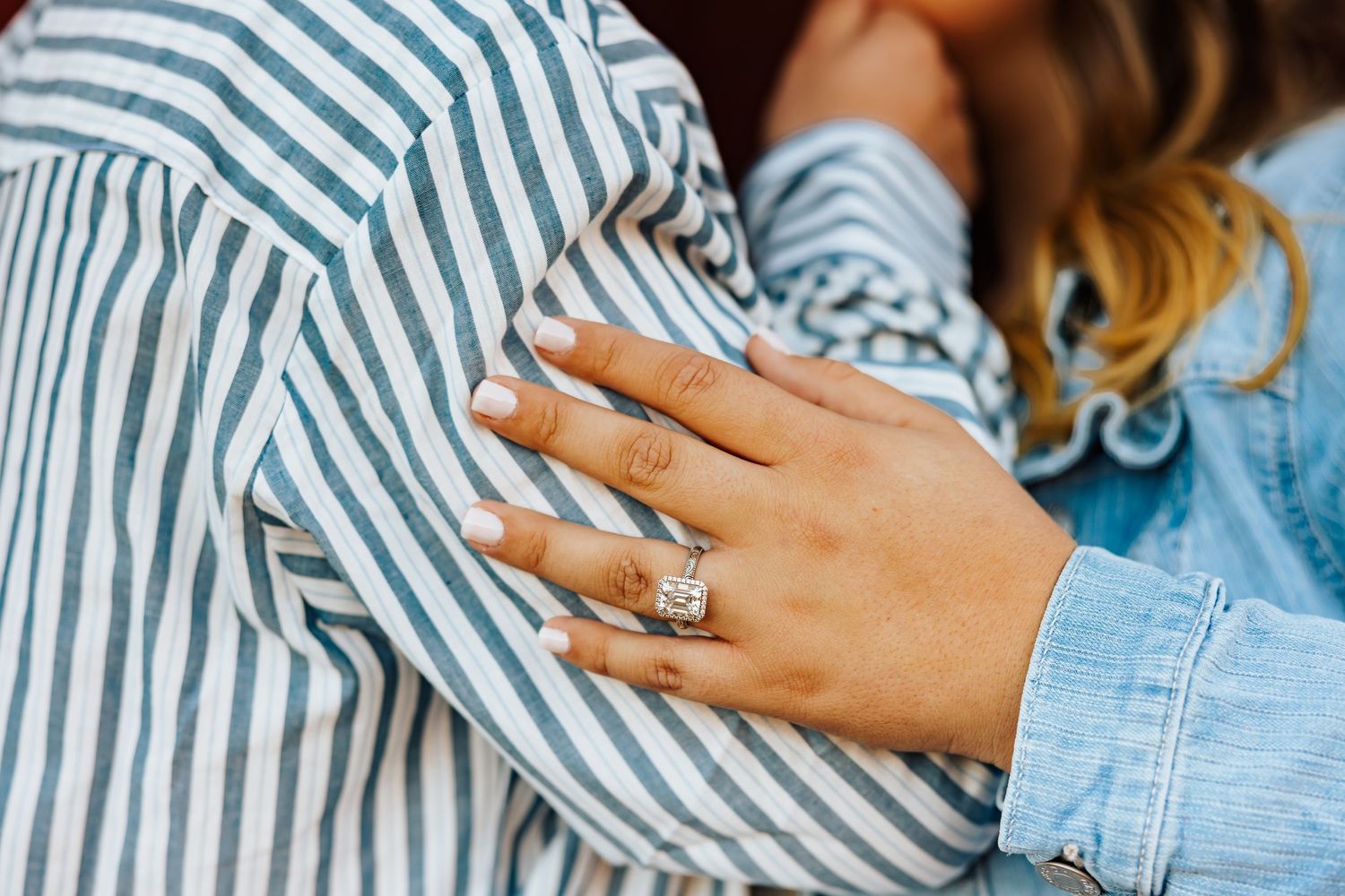 Hands wearing engagement rings touch tenderly during a golden hour photo session.
