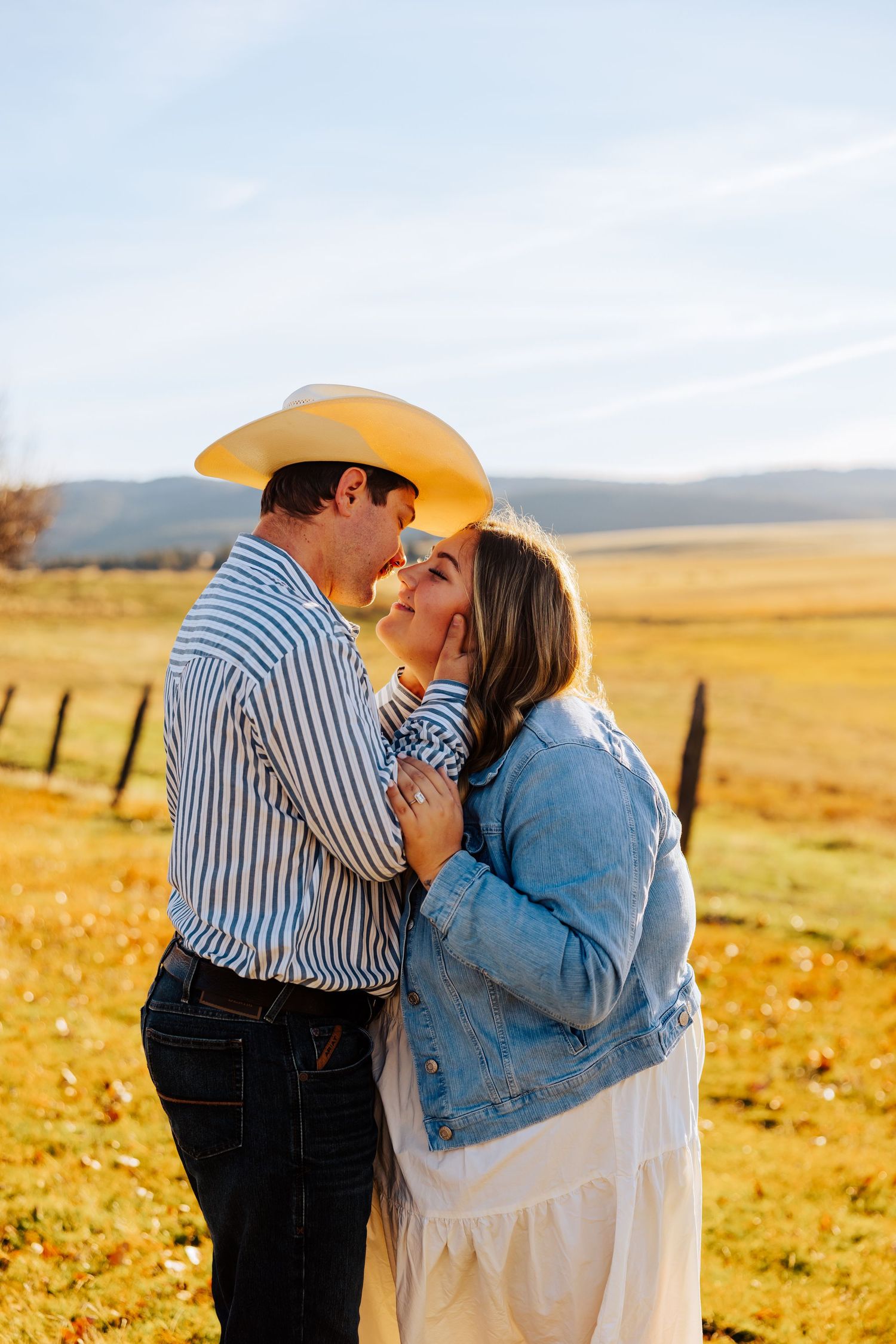 A romantic moment between couple in western wear against backdrop of rolling hills.