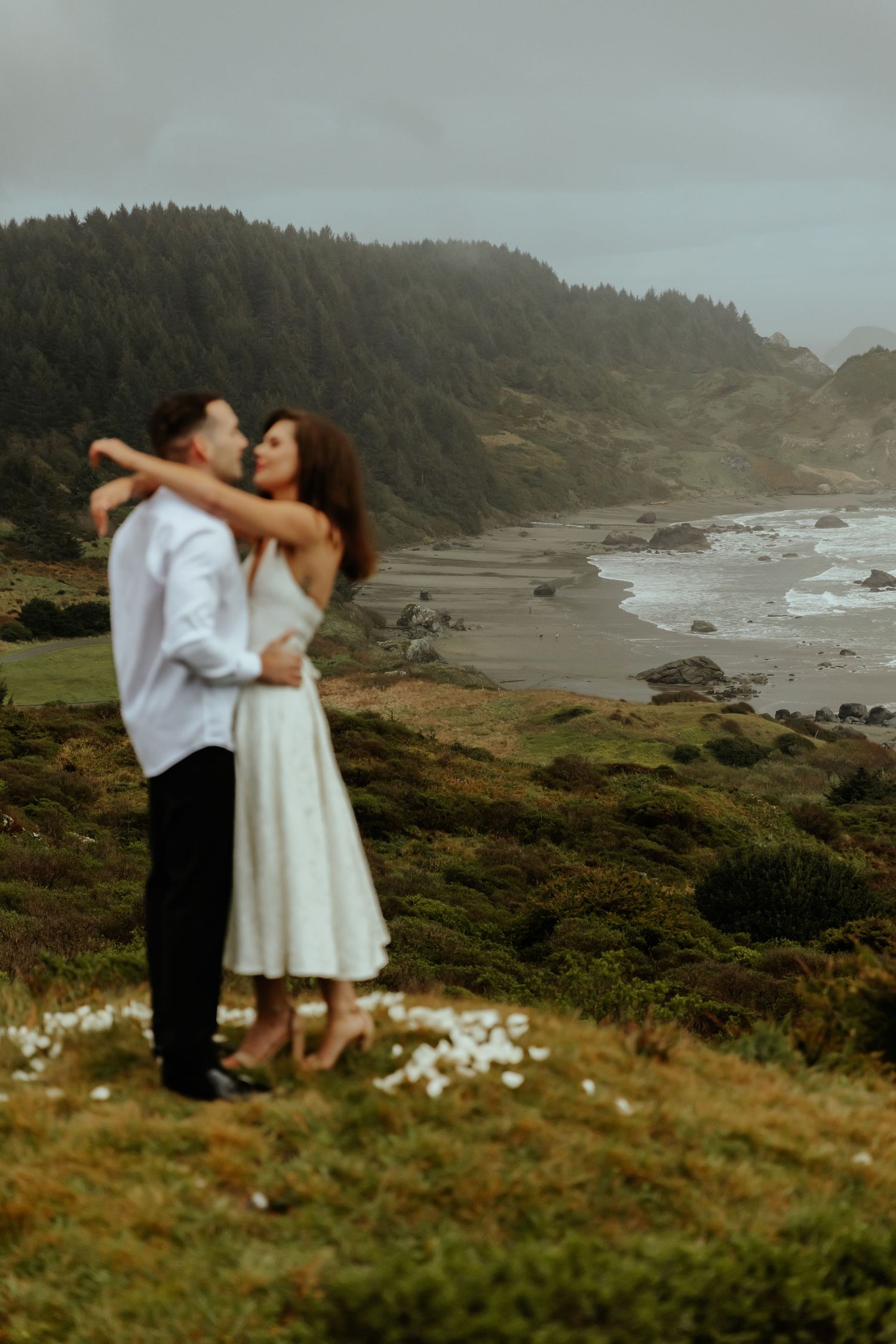 Romantic embrace on a windswept coastal cliff with dramatic ocean views and rocky shoreline.