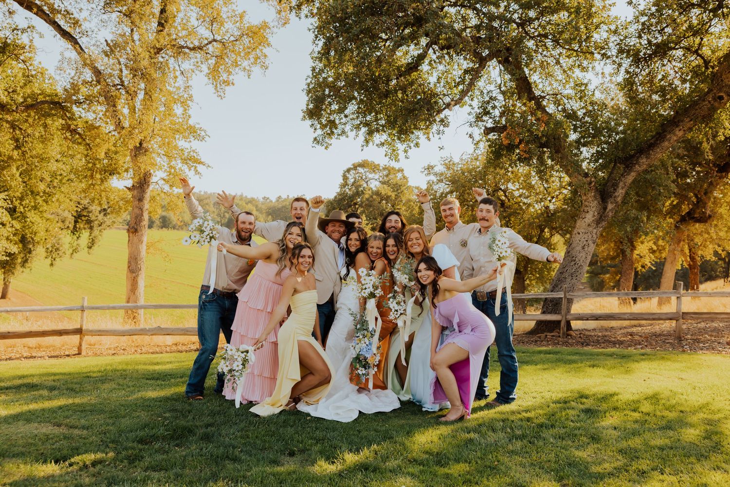 Wedding group photo with guests gathered under golden autumn trees at sunset.