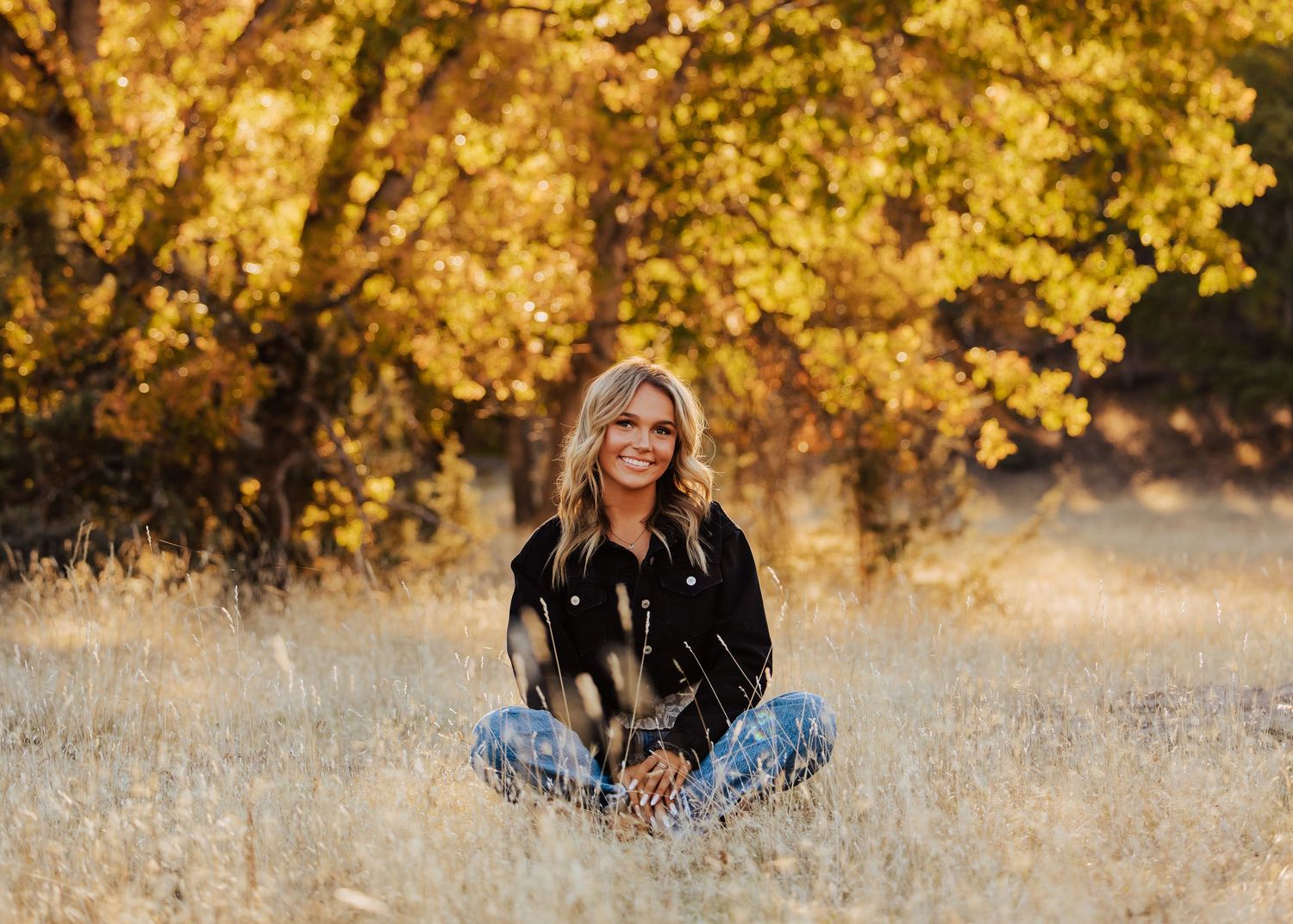 Natural light portrait session with autumn trees and golden grass in the background.