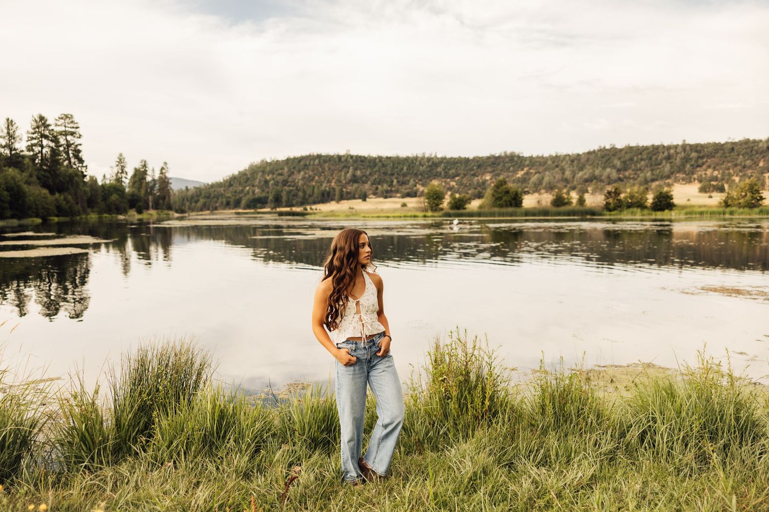 Scenic lakeside landscape with rolling hills and evergreen forests in the background.