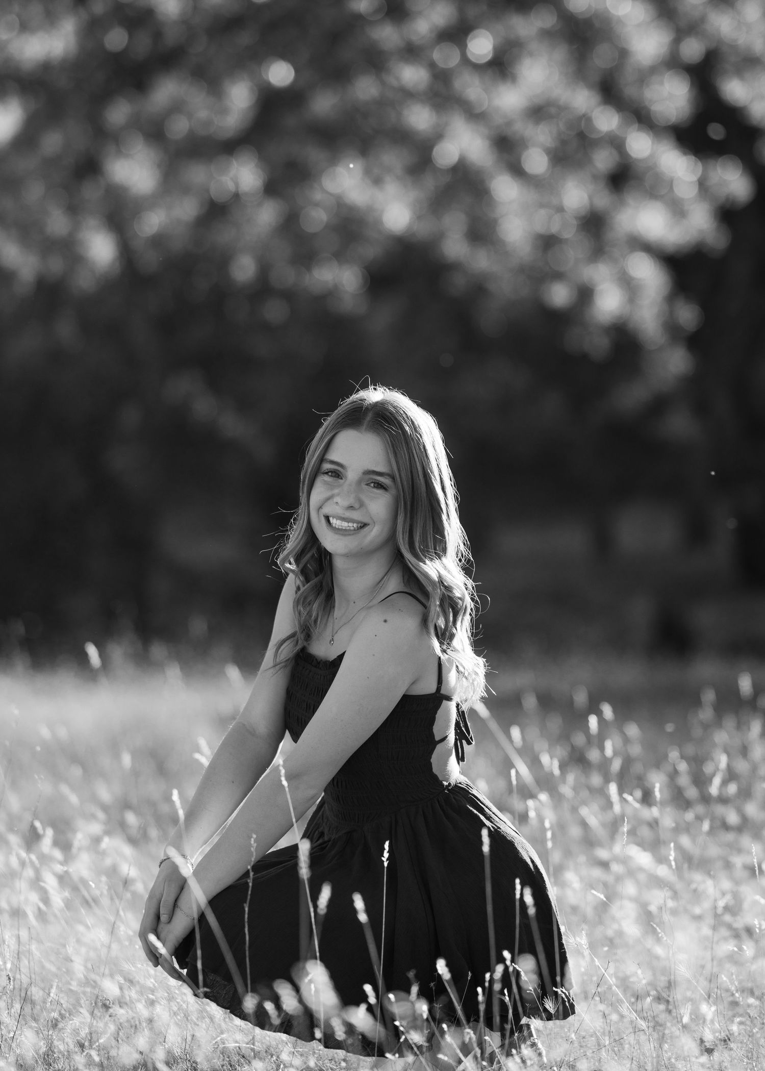 A black and white photo of someone posing in a field of wildflowers with soft lighting.