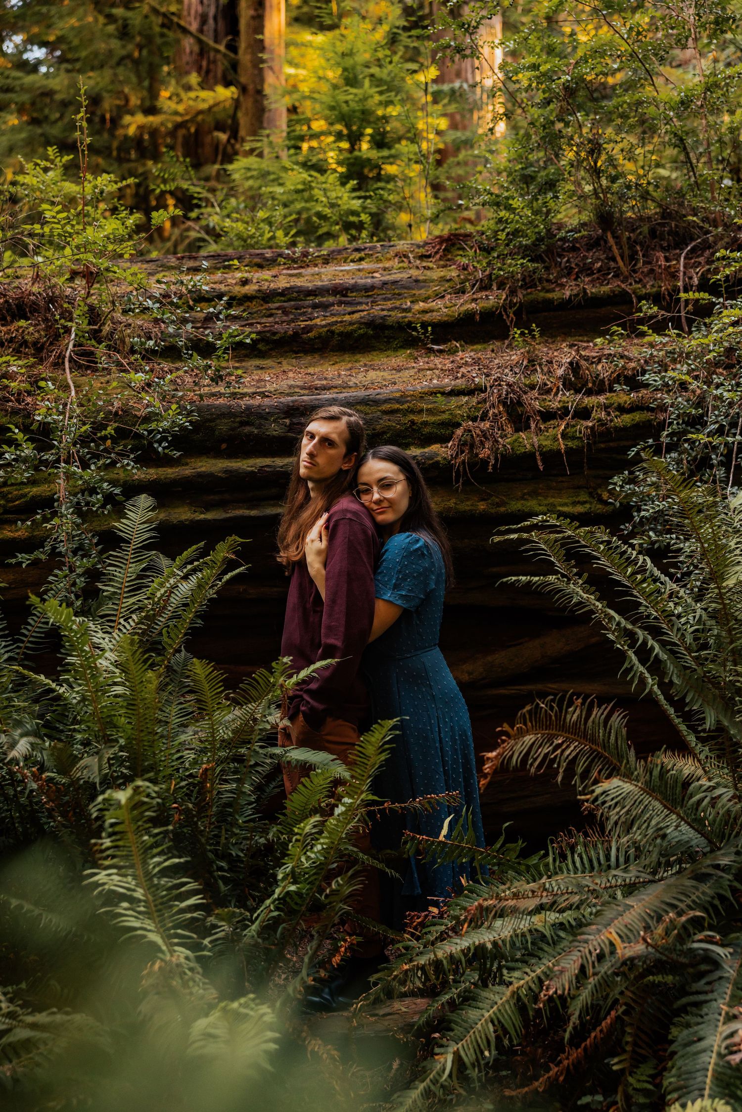 Romantic couple's portraits among ferns and redwoods in a moody forest setting.