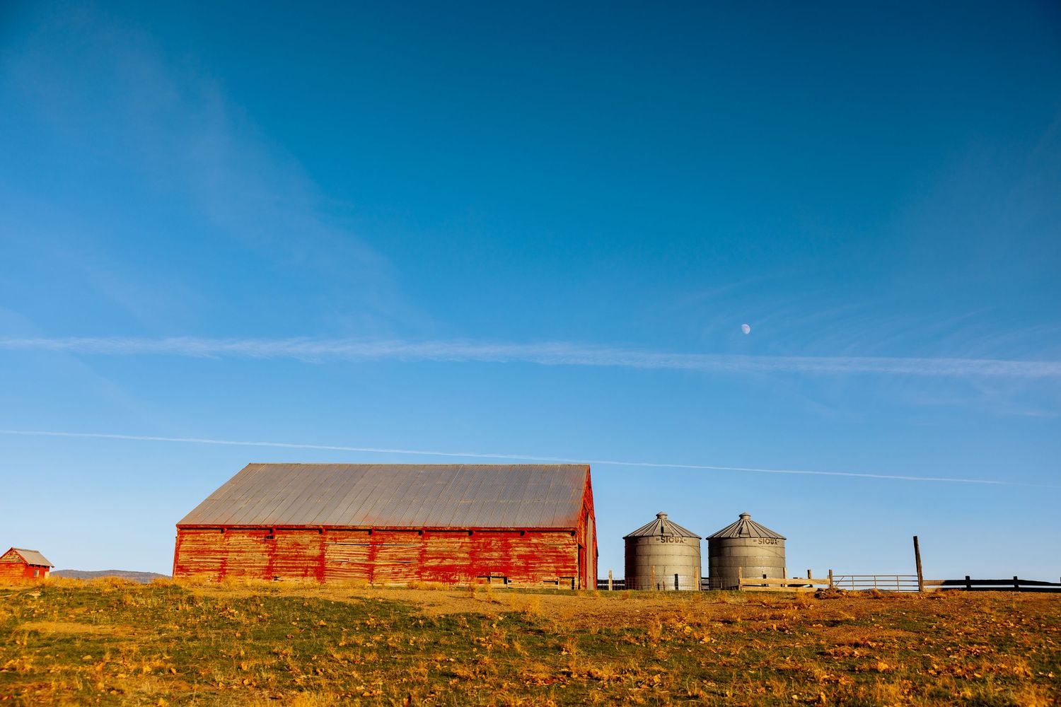Rural landscape with grain silos and farm buildings under a bright blue sky.