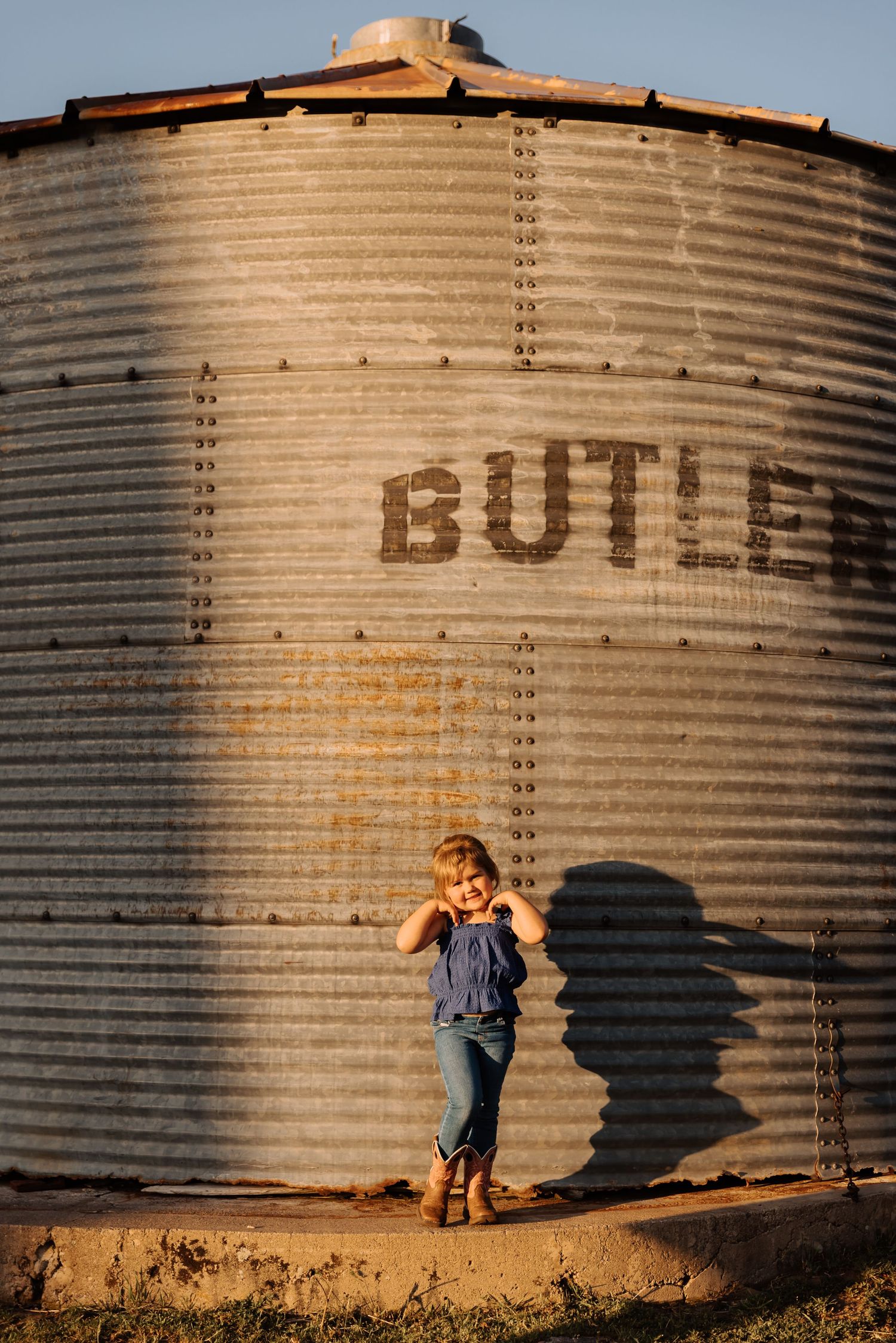 Series of photos showing a child playing near large metal grain silos at golden hour.