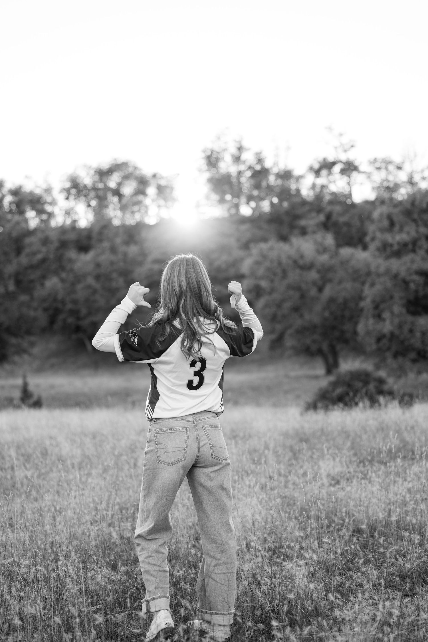 A black and white photo showing someone from behind wearing jeans in a sunlit field.