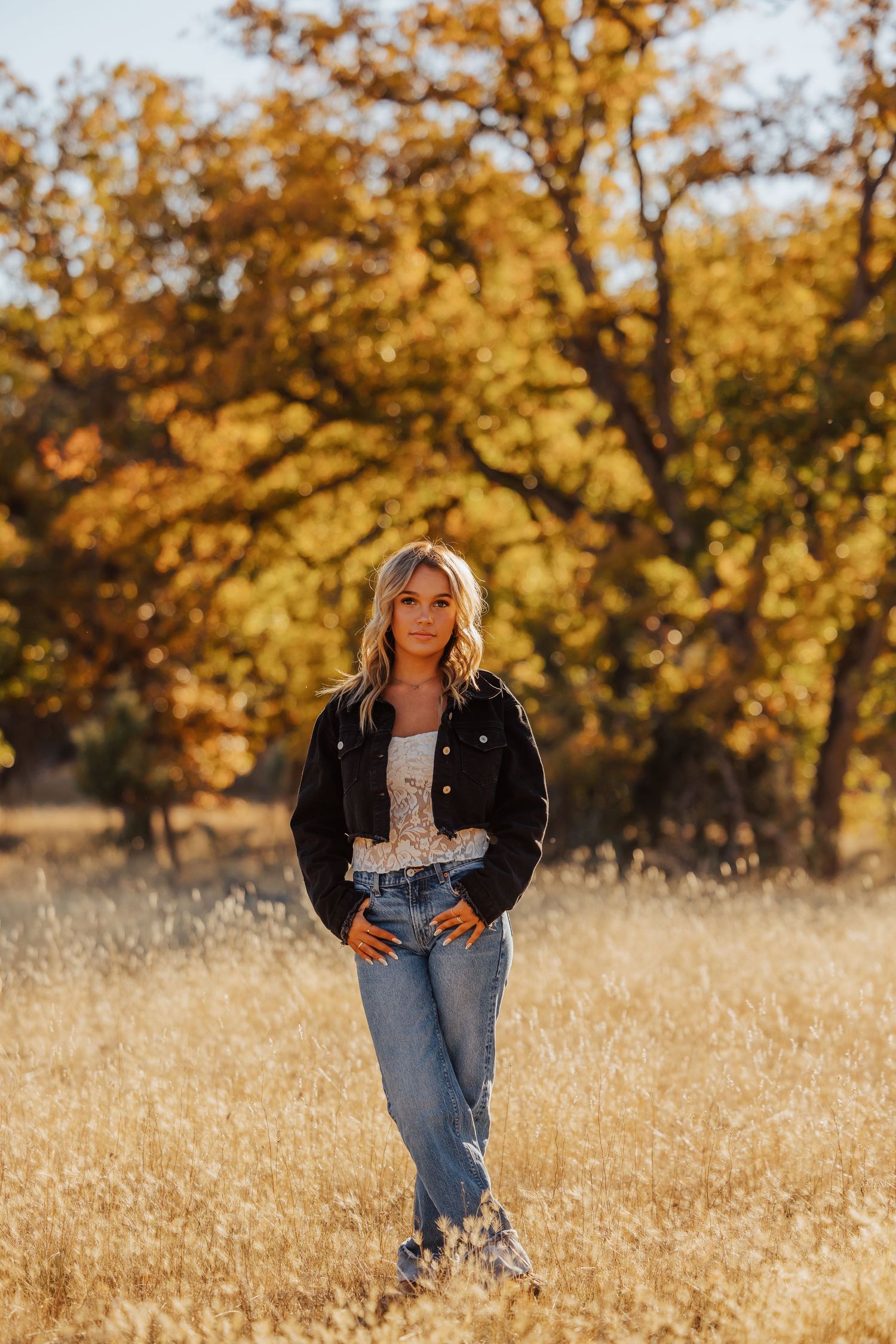 Autumn portrait session in a field with golden trees and tall grass.