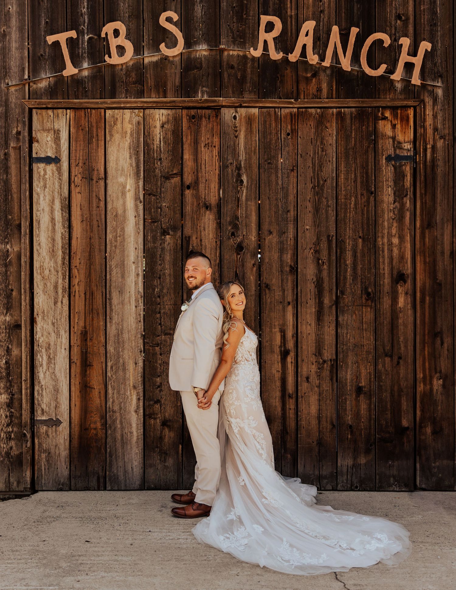 Wedding couple posing against rustic wooden barn wall with vintage ranch signage.