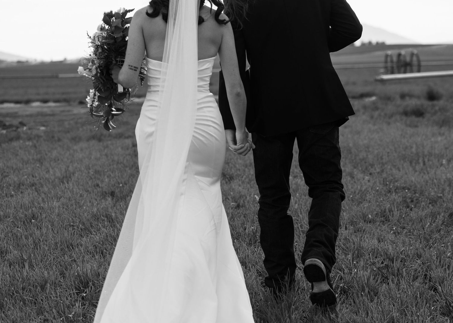 Black and white photo of a couple walking through a field on their wedding day.