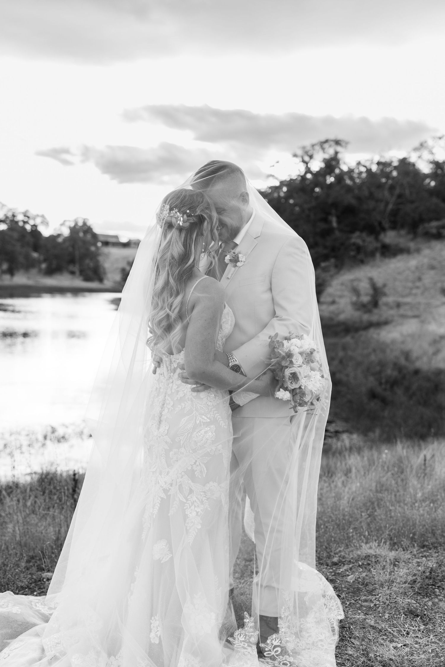 Black and white wedding portraits capture intimate moments between newlyweds by a lake.