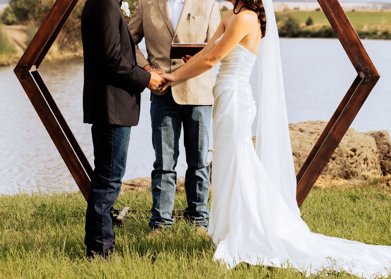 Wedding ceremony setup with rustic wooden arch and white chairs outdoors.