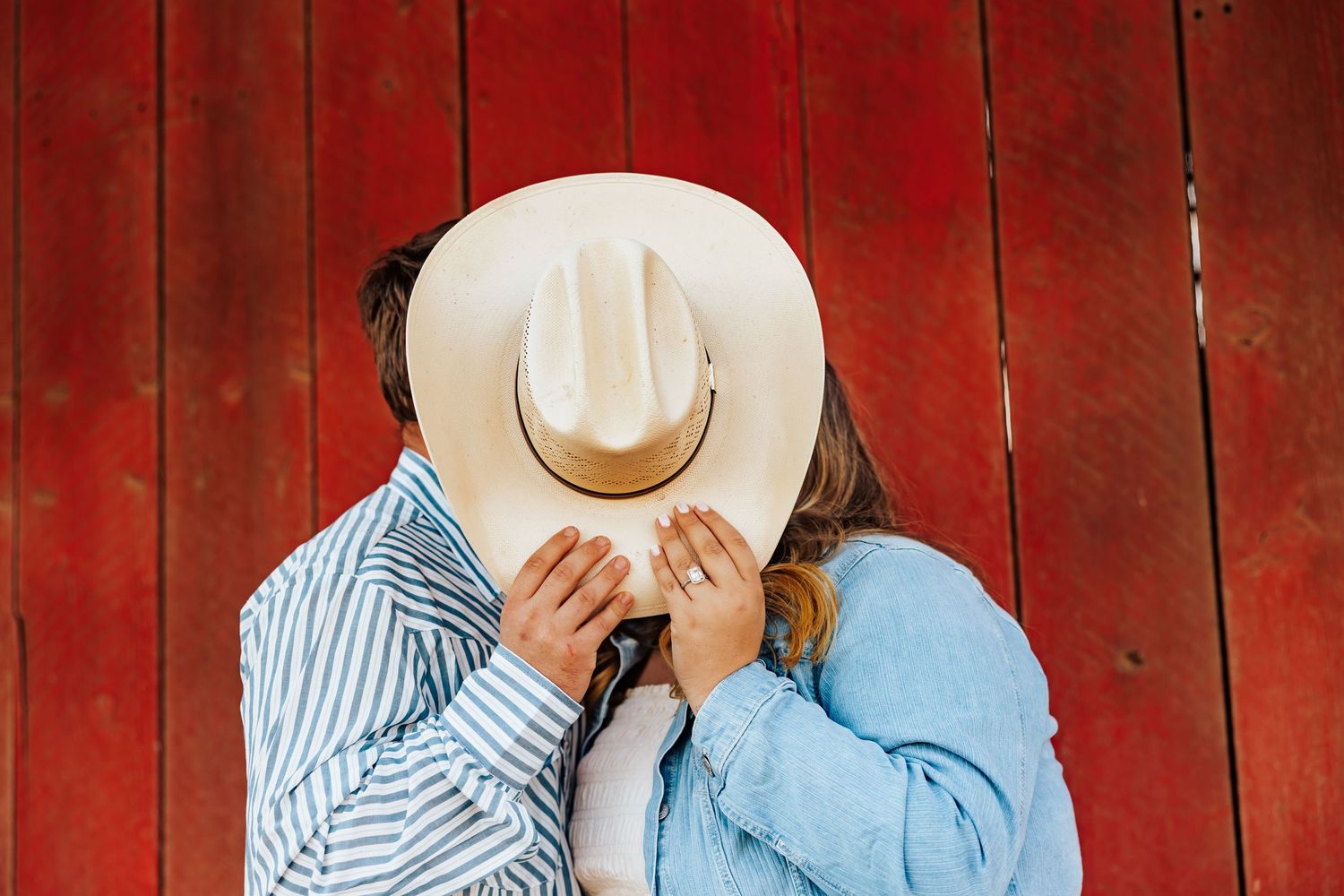 A couple embraces against a rustic red barn wall during a romantic photoshoot.