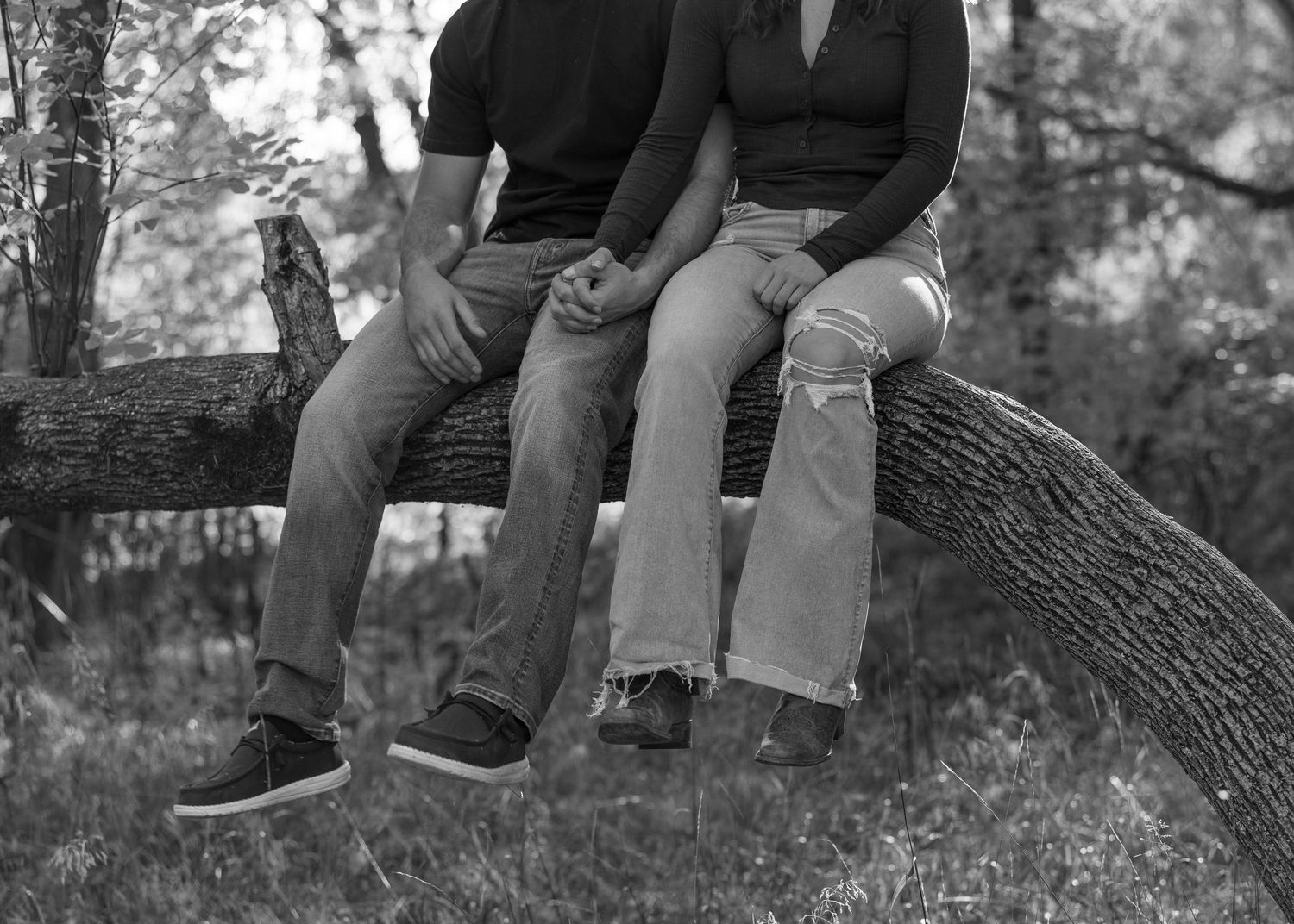 Black and white photo of people sitting together on a large tree branch.