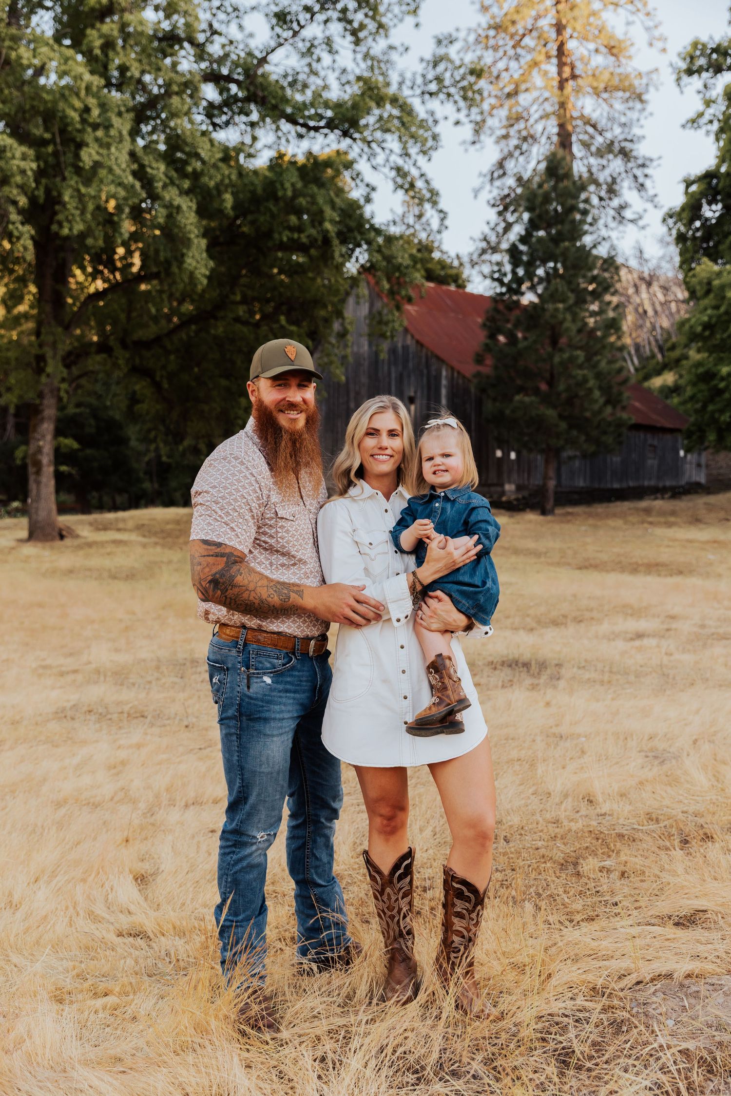 A family shares a tender moment in a golden field with an old barn behind them.
