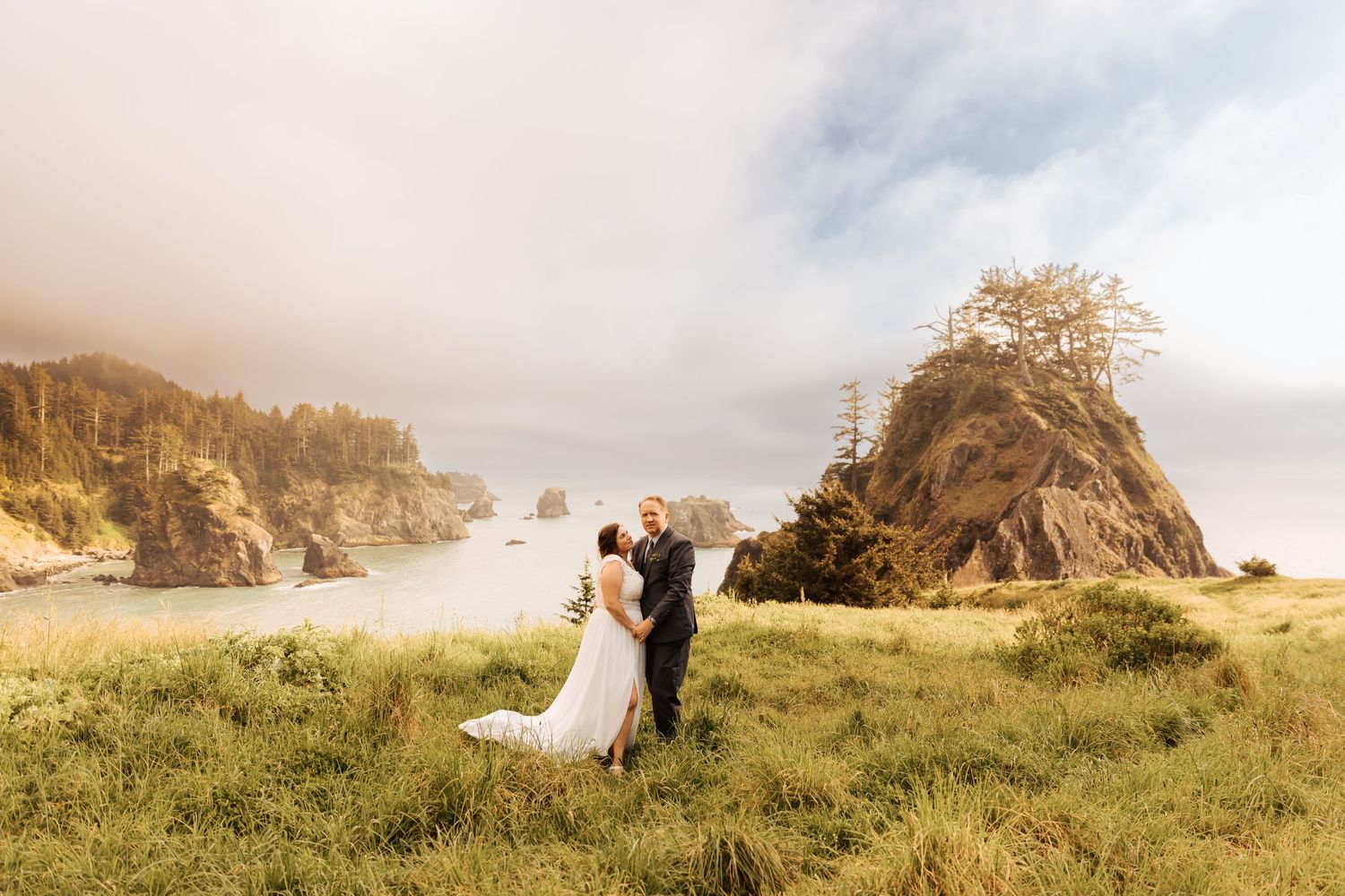 Wide landscape view of couple on grassy coastal cliffs during wedding.