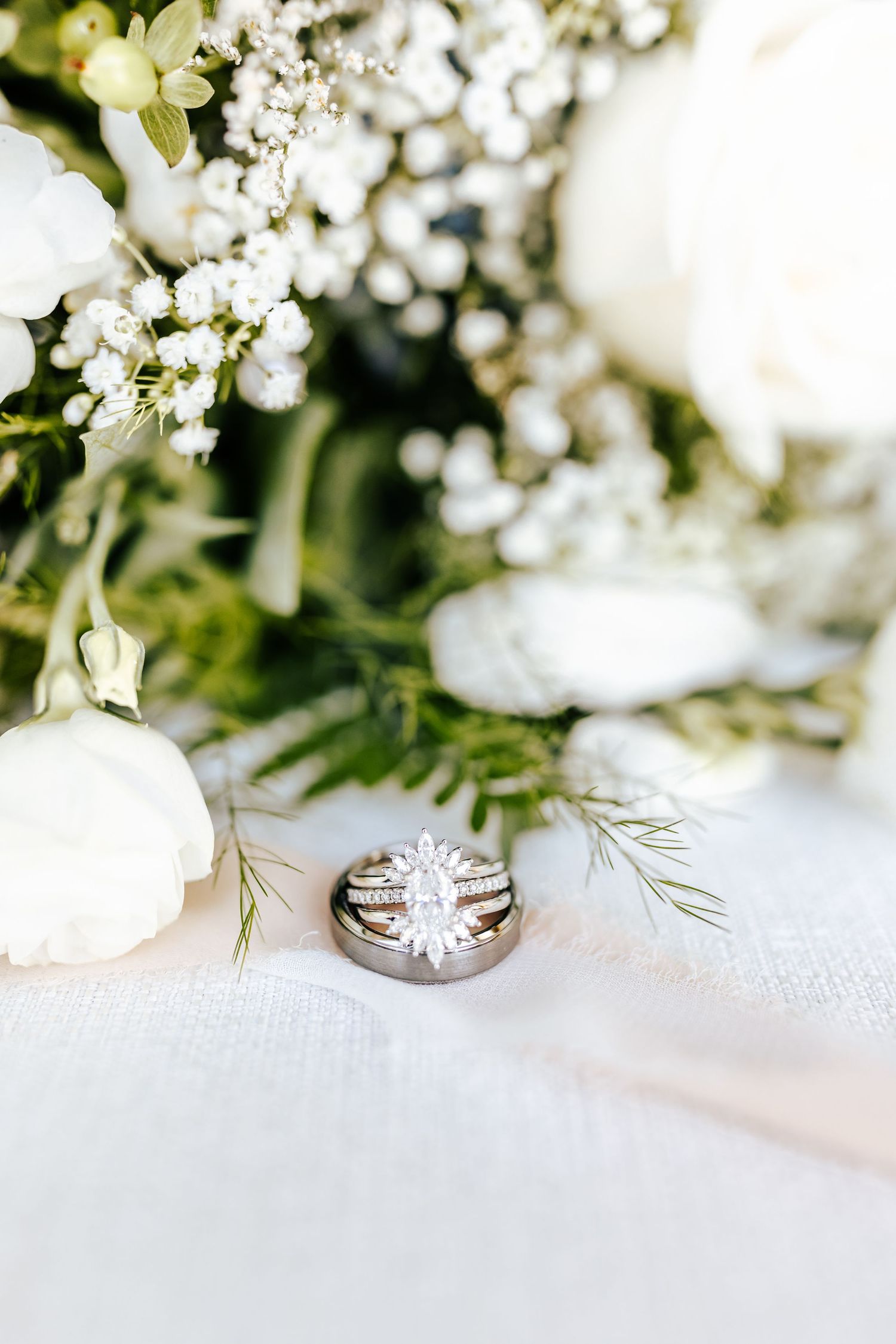 Delicate white flowers and wedding rings arranged on white linen.