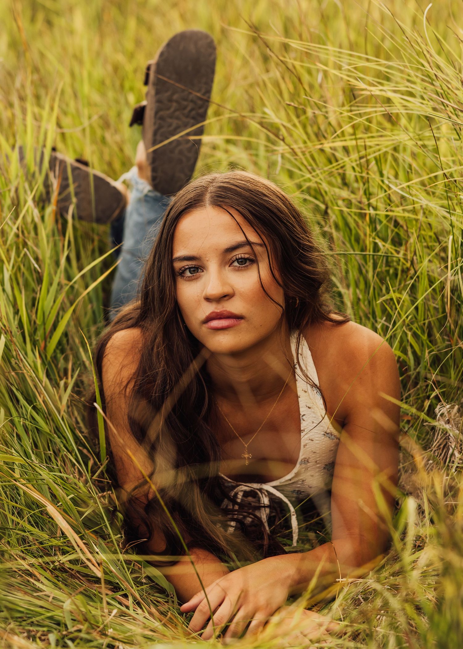 A person in casual attire lies in tall golden grass during a summer photoshoot.