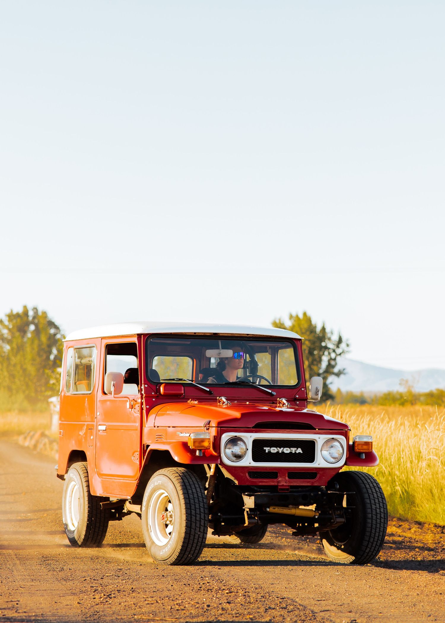 Two vintage orange Toyota FJ40 Land Cruisers parked on a dirt road in a rural setting.
