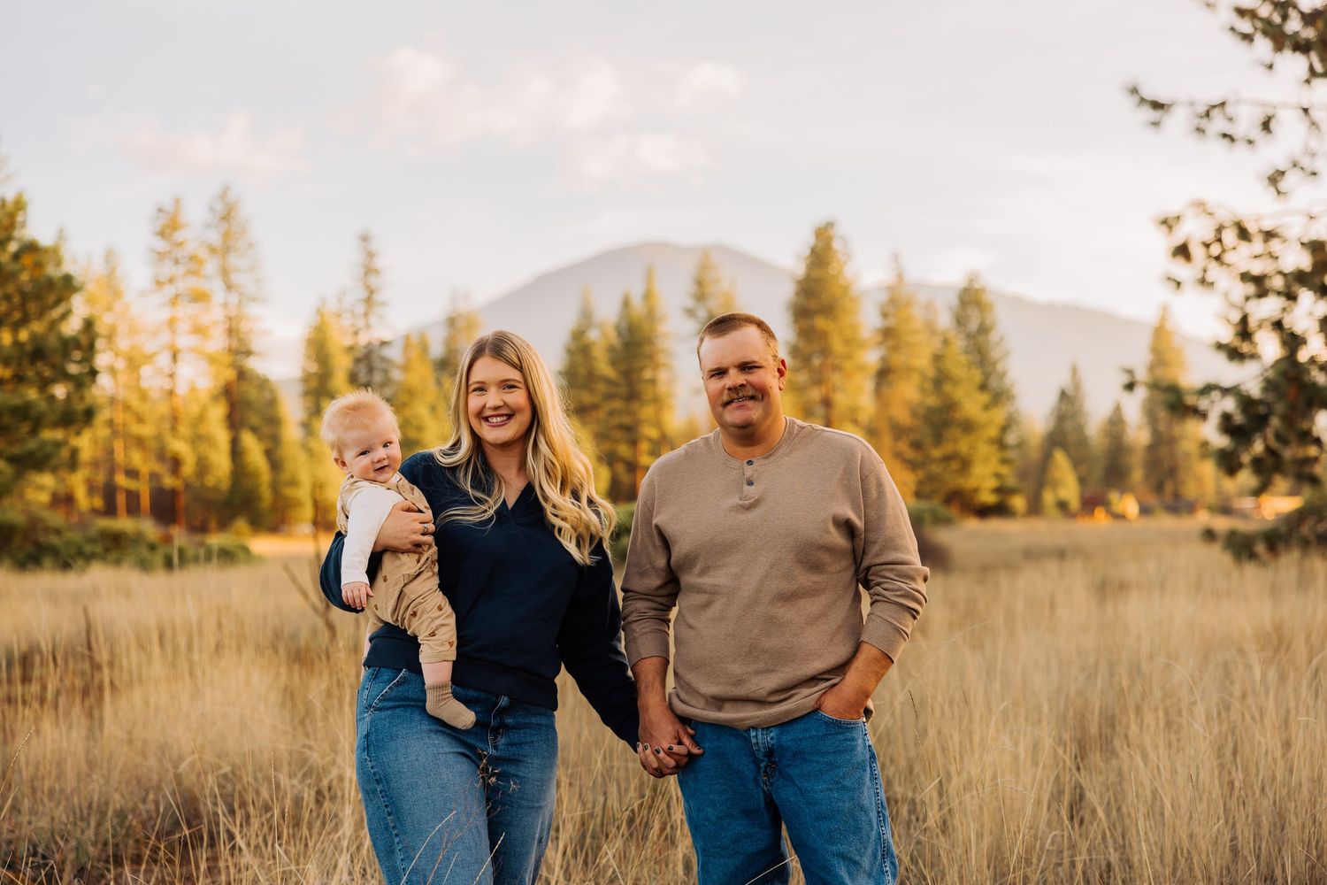 Family laughing together in autumn field with pine trees and mountains.