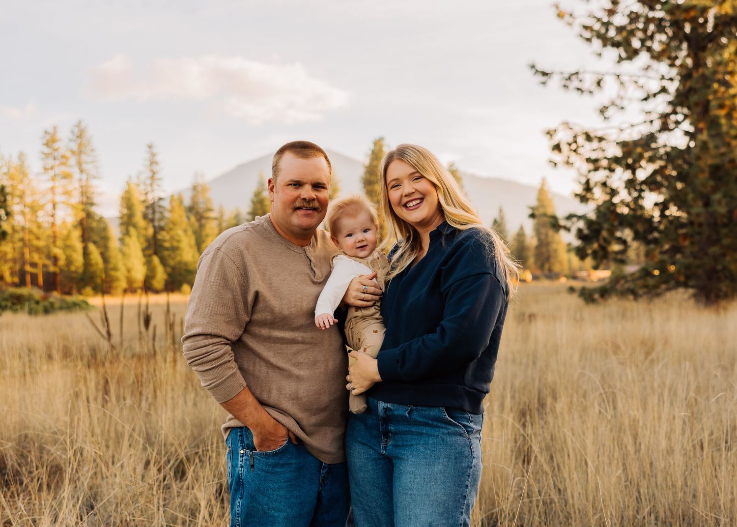 Family enjoying autumn sunset in tall grass field with mountain backdrop.
