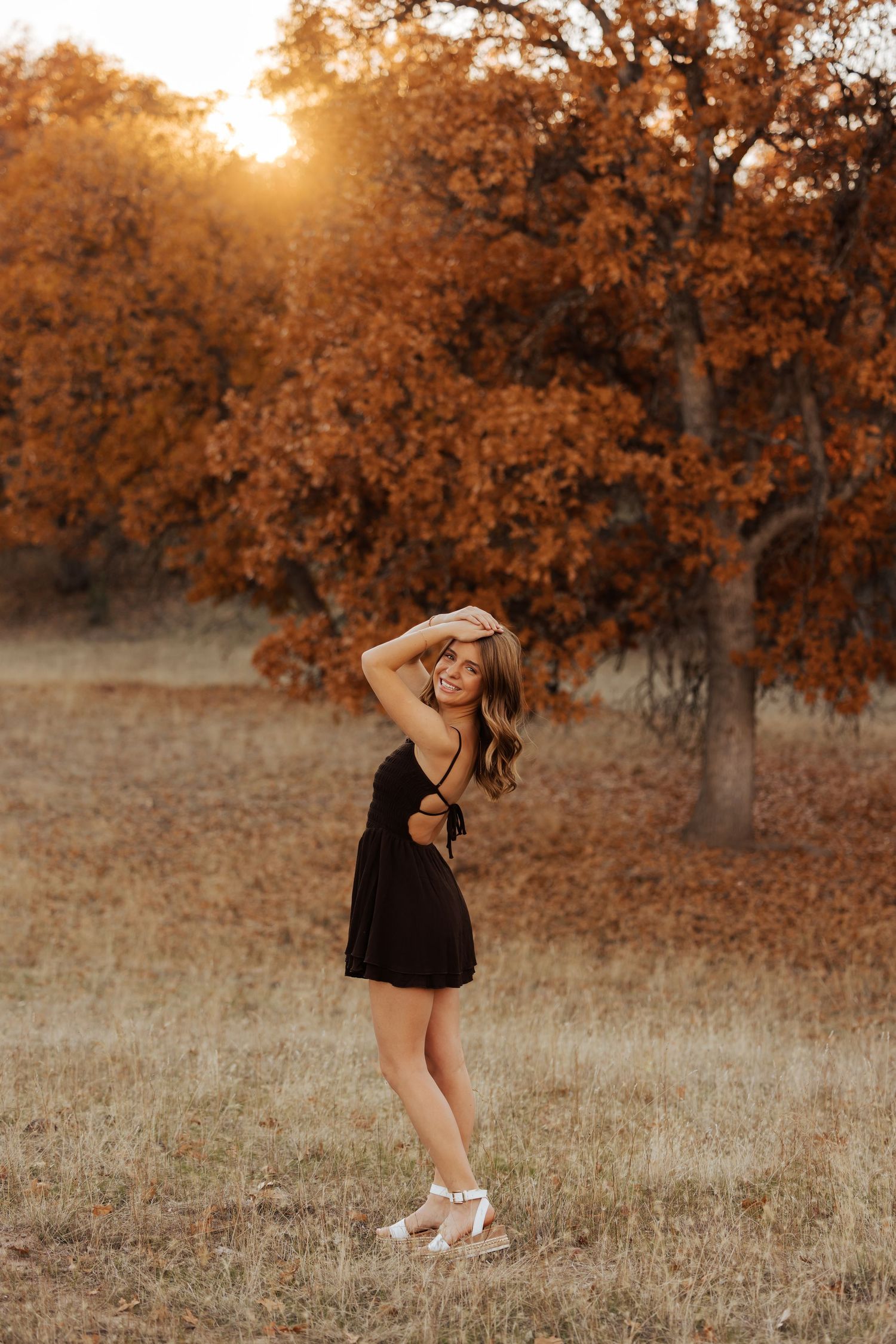 Lifestyle portrait session in a field with autumn trees and golden hour lighting.