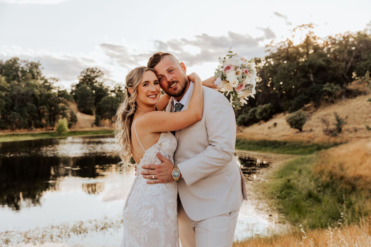 Wedding couple poses together near scenic lake during golden hour.