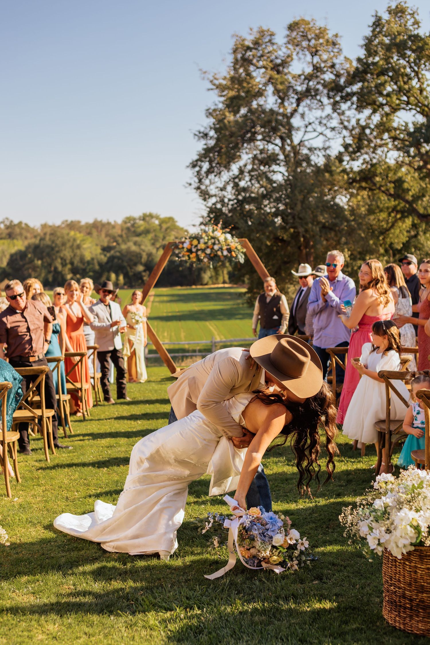 Wedding guests enjoy a lively outdoor celebration under oak trees at sunset.