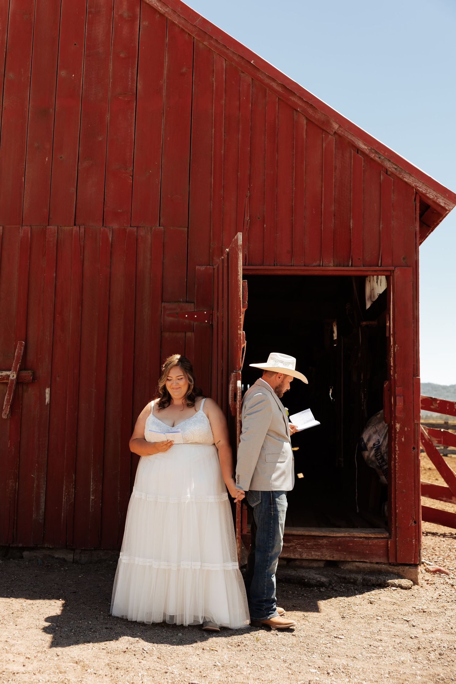 Bride and groom holding hands outside a rustic red barn during a country wedding ceremony.