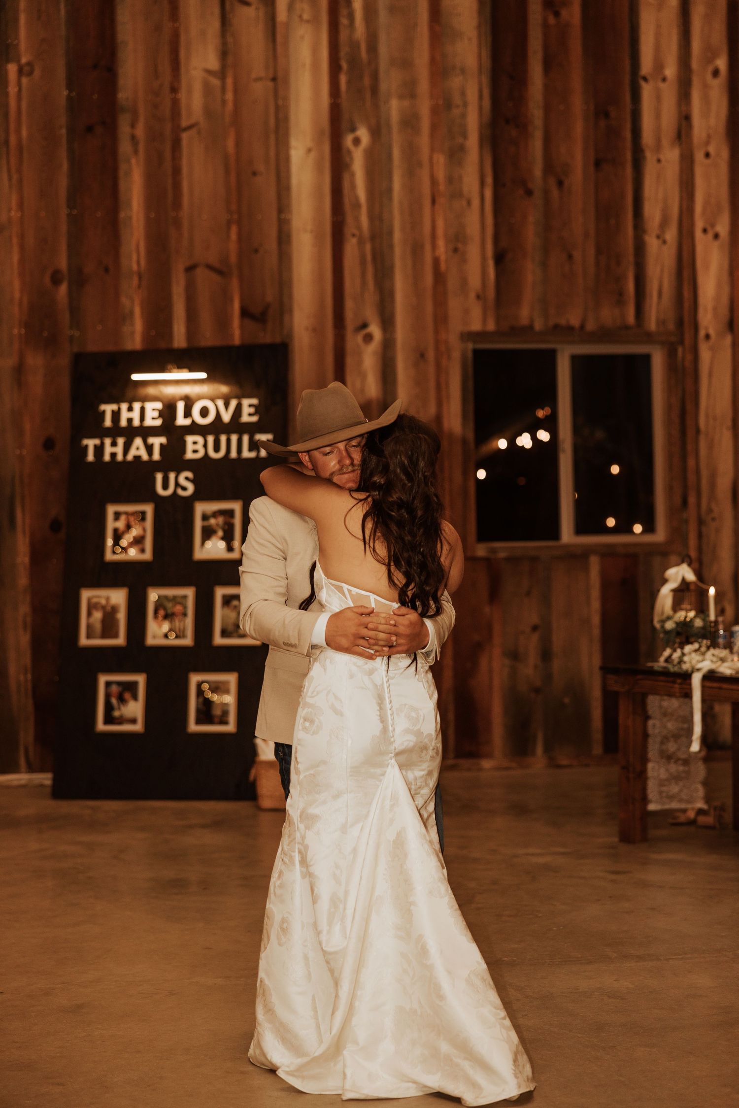 Romantic dance between newlyweds in a rustic wooden barn with string lights and decorative signs.