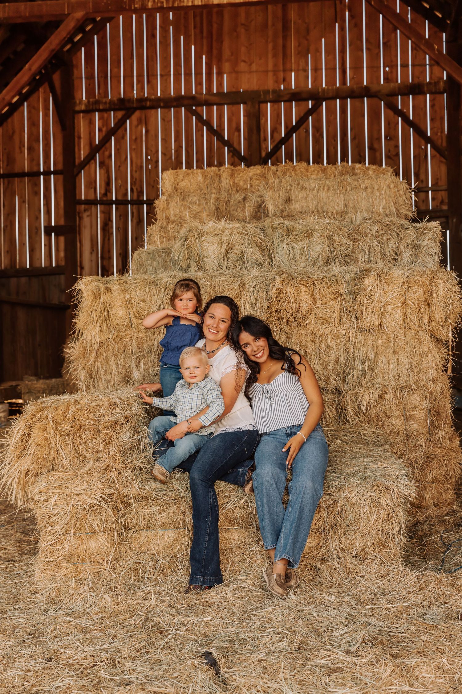 A family relaxes together on stacked hay bales inside a wooden barn.