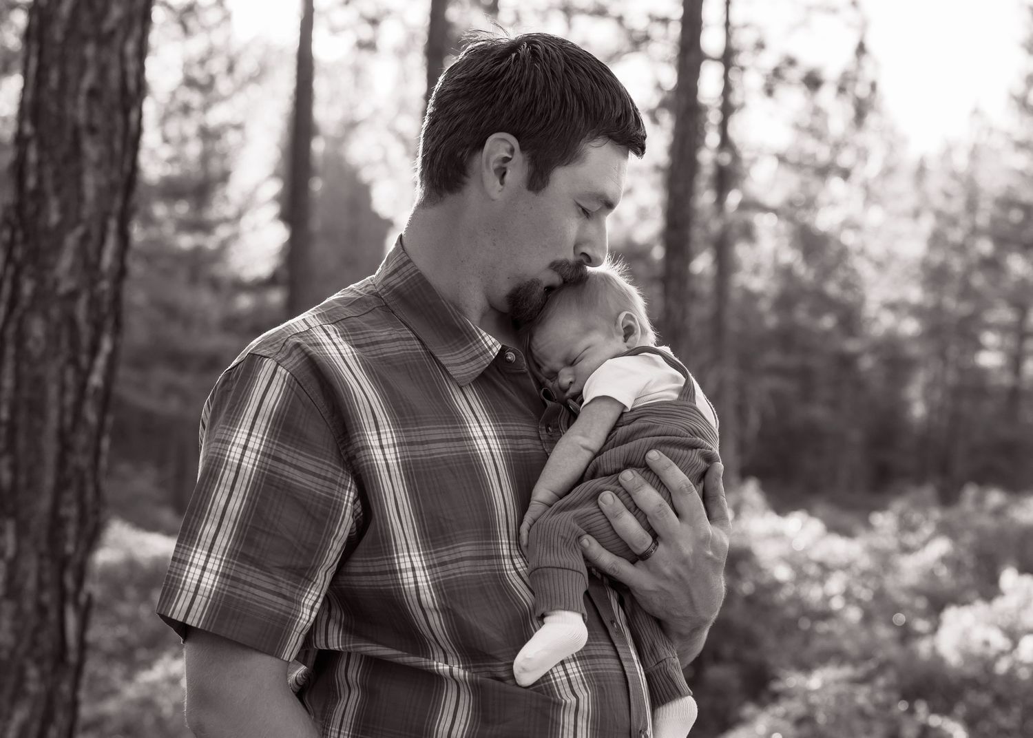 Black and white portrait of a father tenderly holding a newborn baby against his chest.