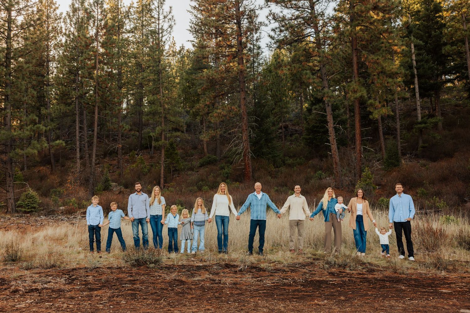 Multi-generational family lined up in coordinated blue outfits against a forest backdrop at sunset.