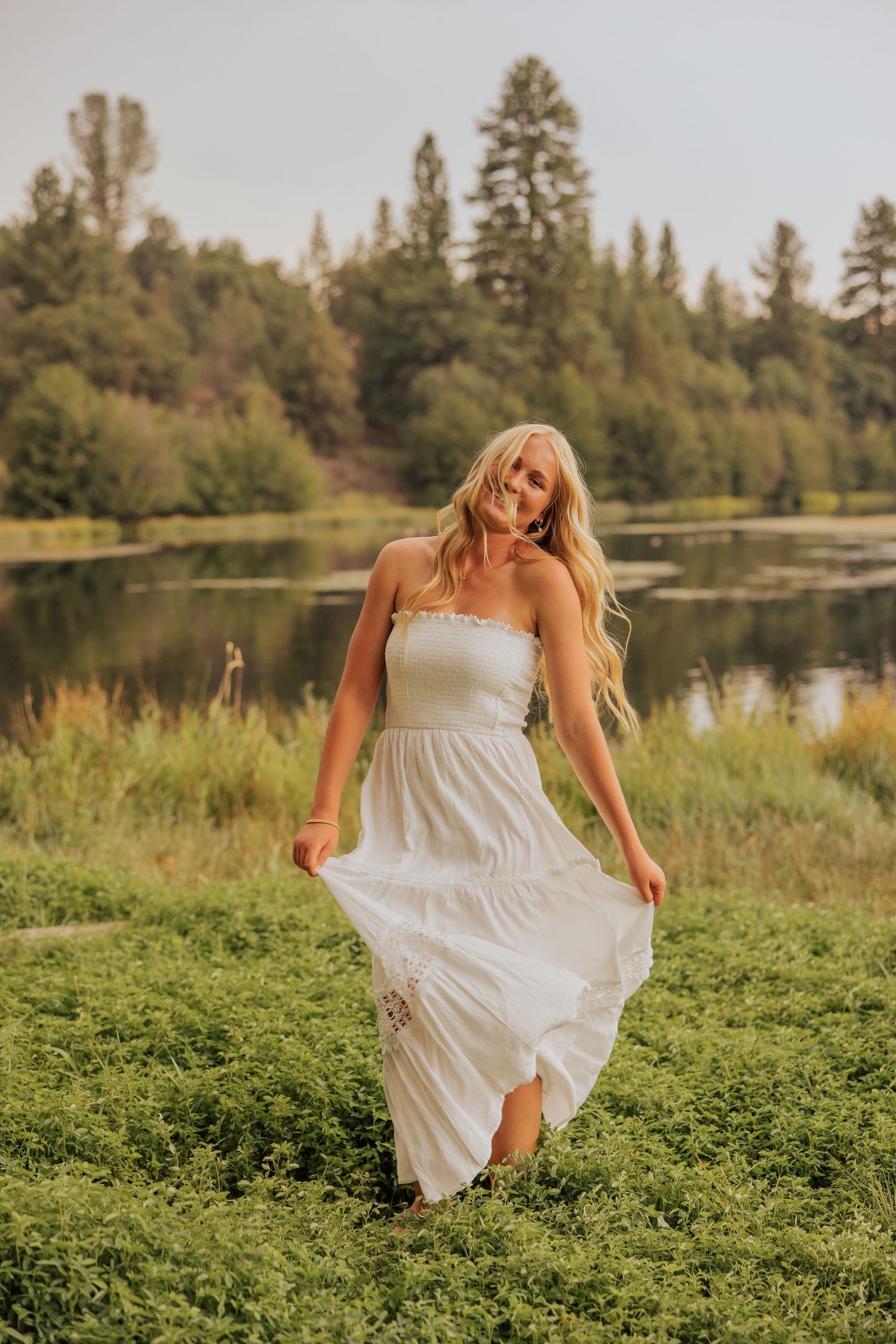 Person in flowing white dress twirling in field by lake during sunset.