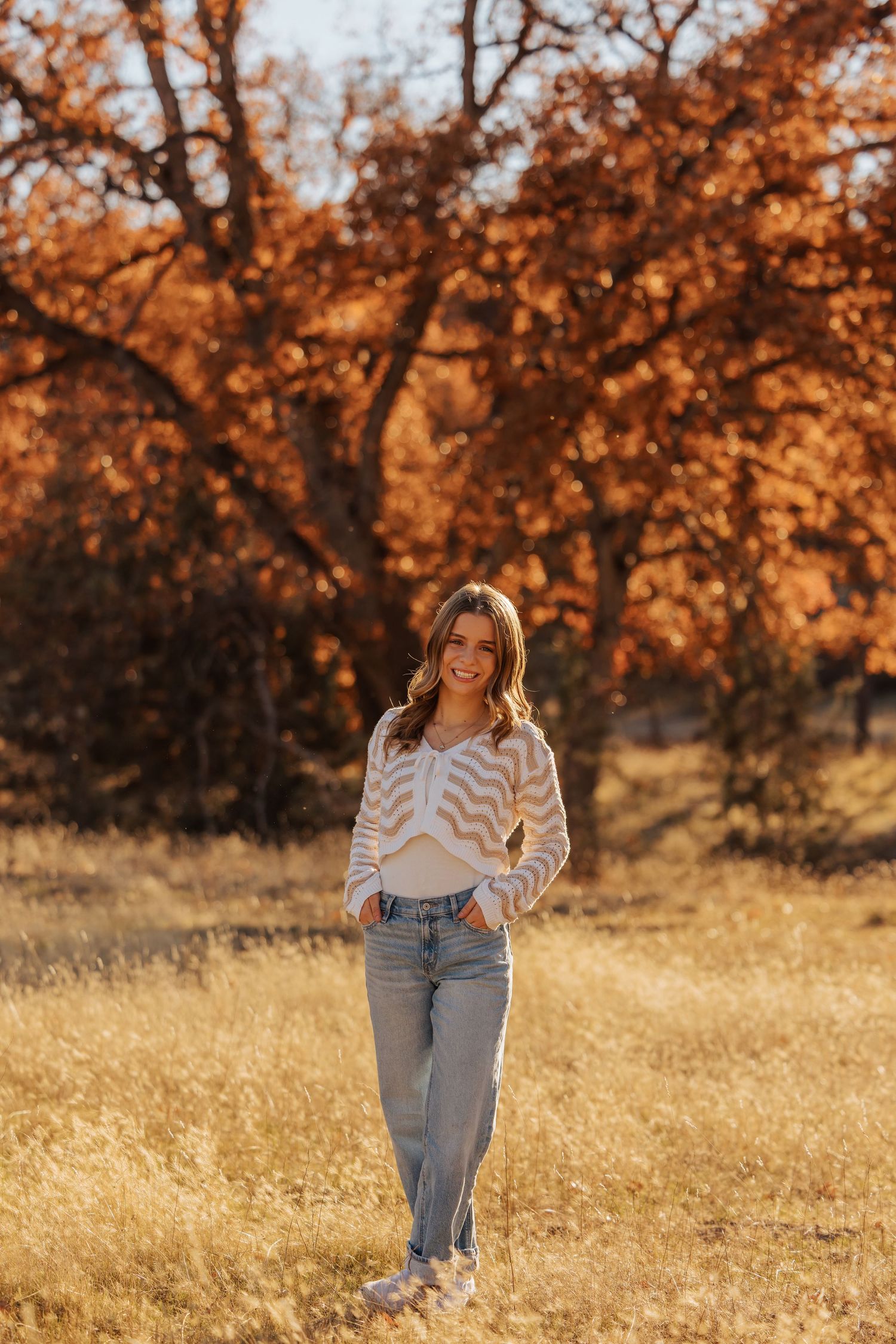 Casual outdoor portraits in denim and white top with fall trees in warm lighting.