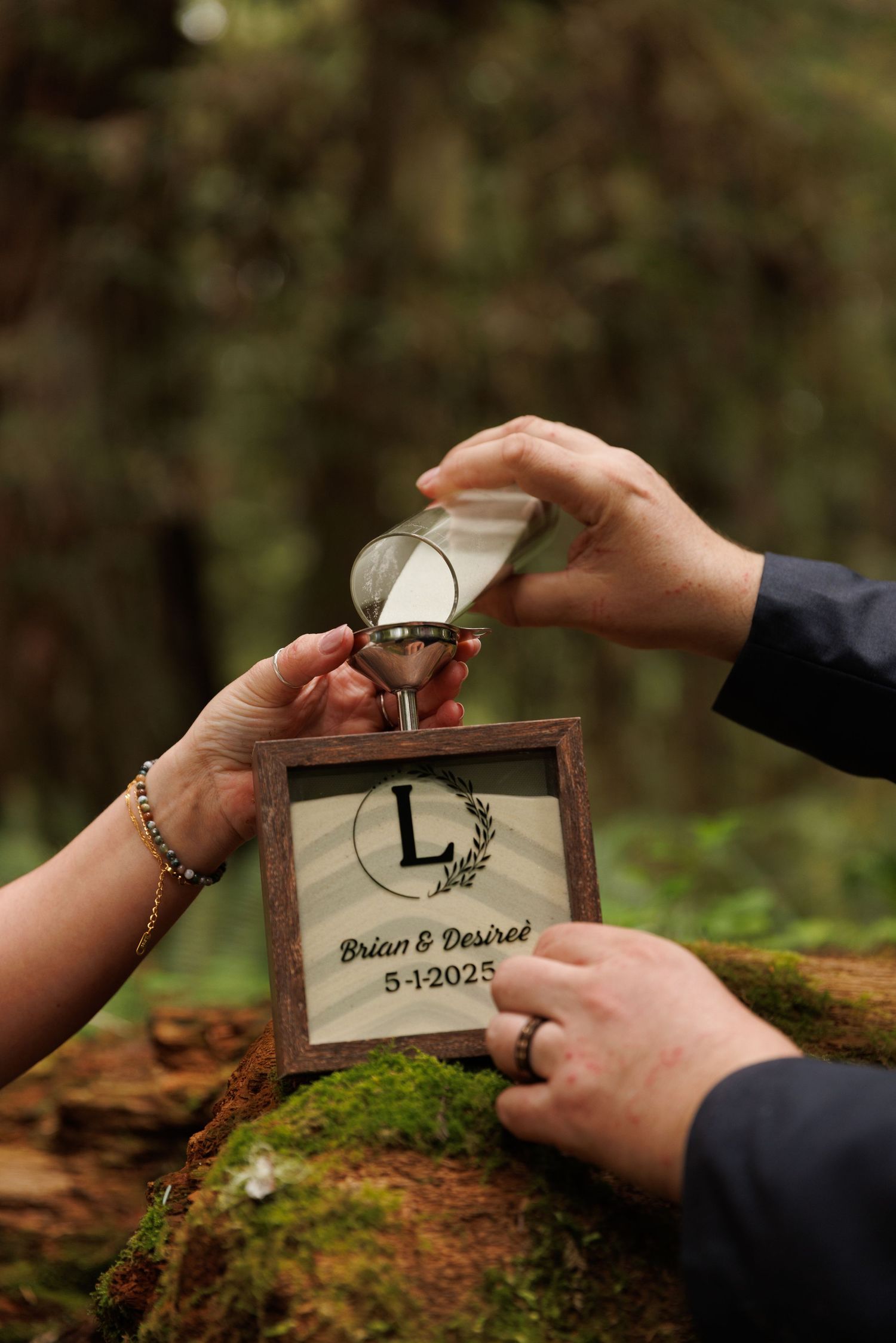 Hands placing wedding date inscription in wooden box against mossy forest background.