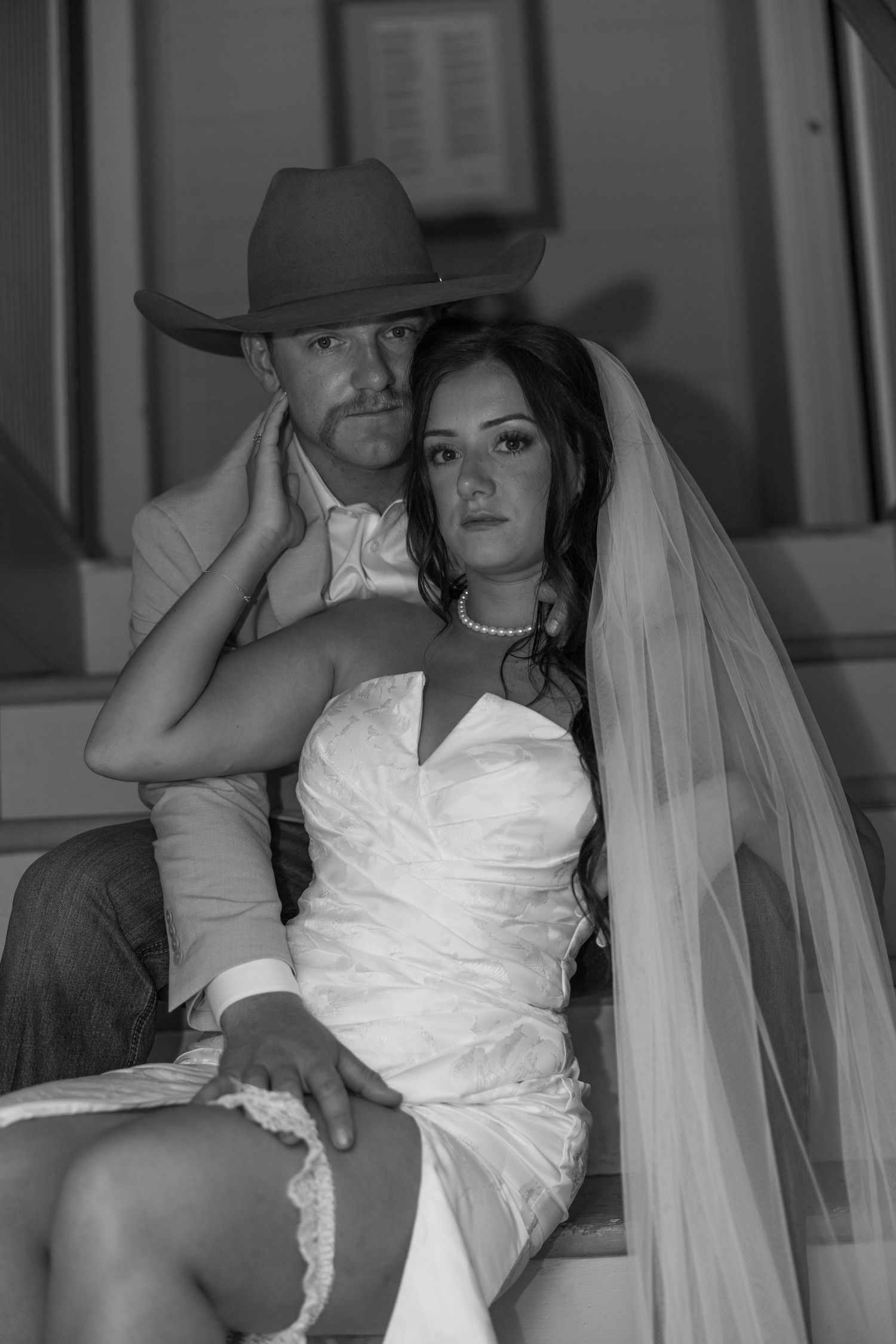 Dramatic black and white portrait of newlyweds in western attire on stairs.