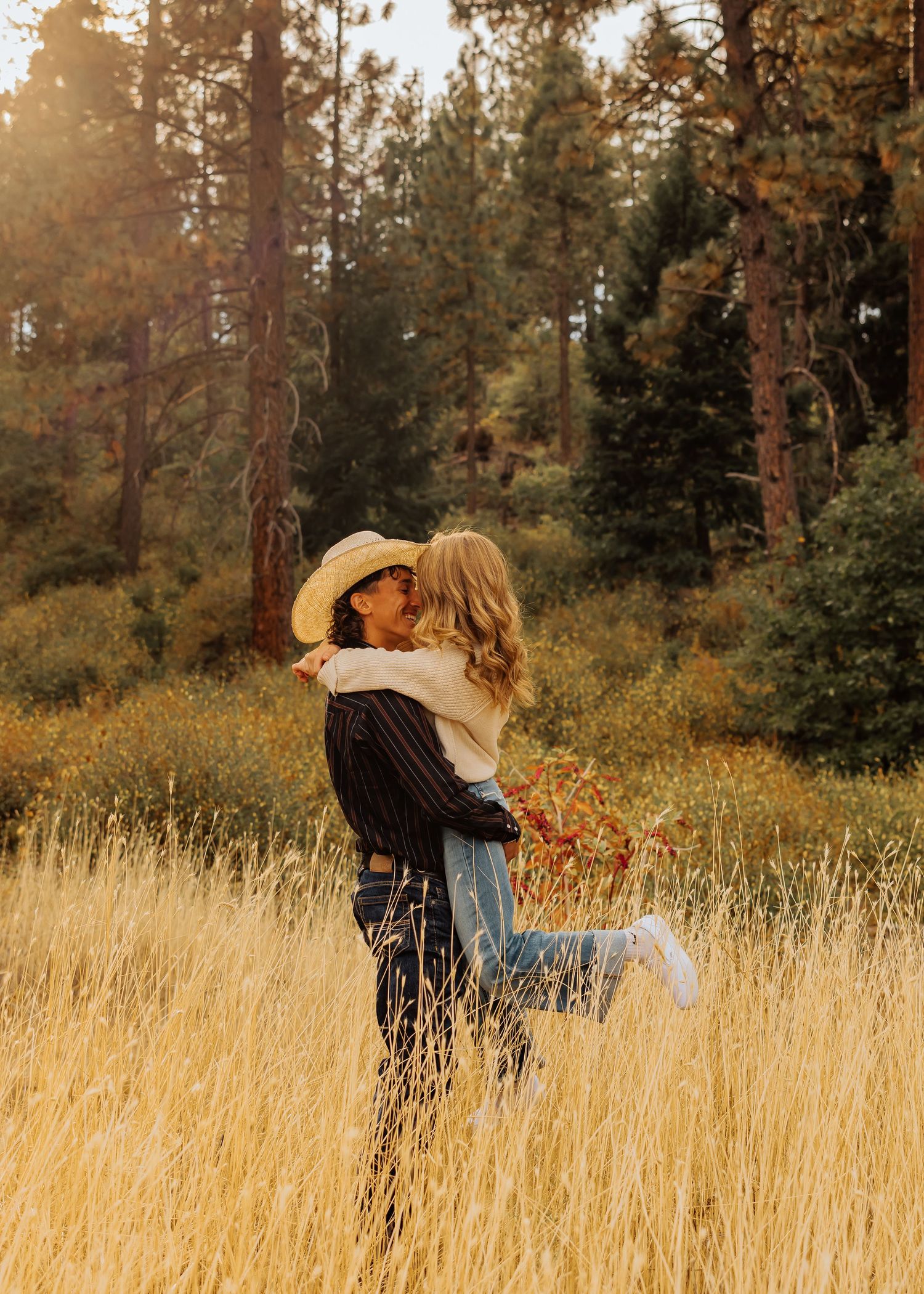 Playful couple dancing and twirling in a tall grass field with autumn colors surrounding them.