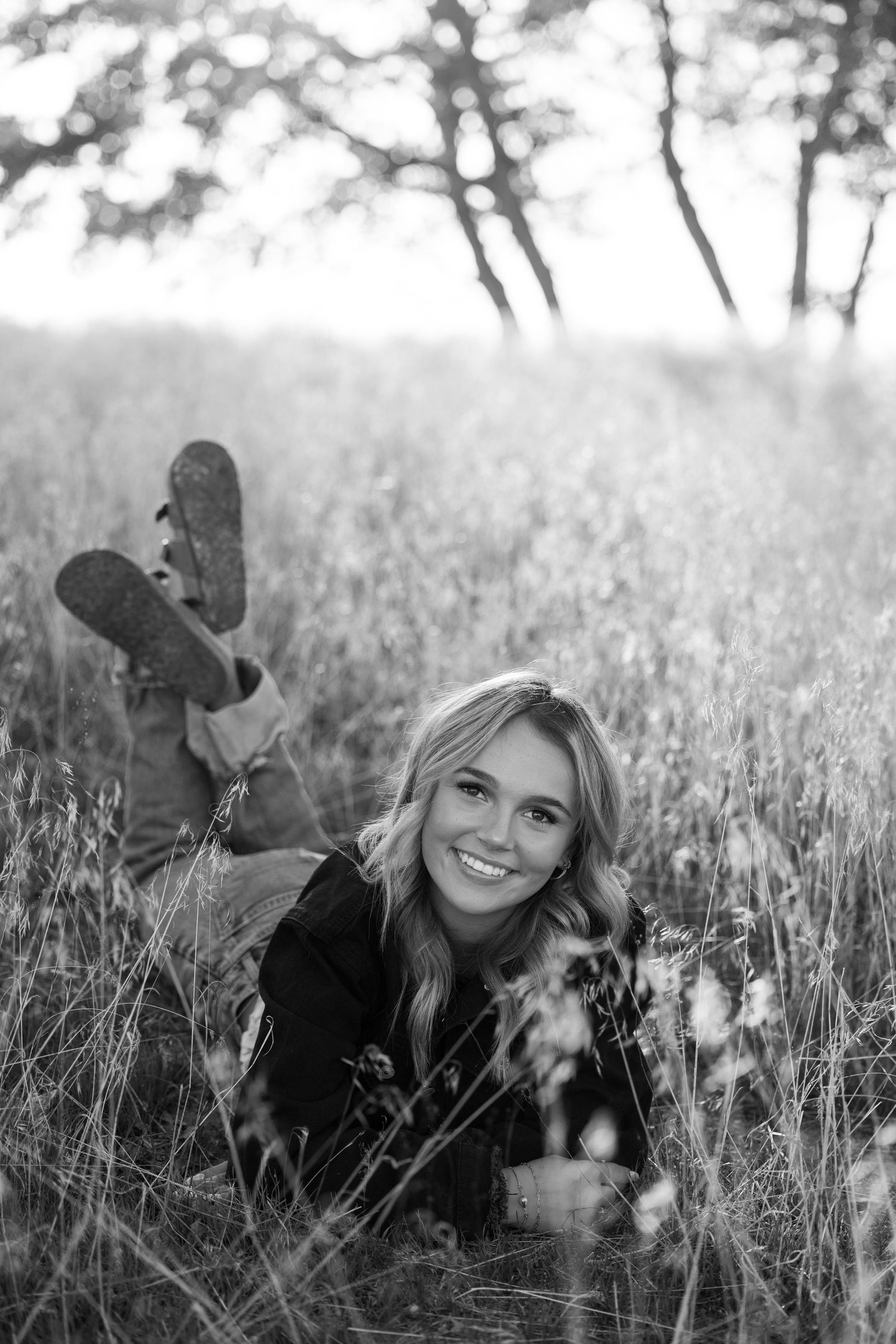 Casual outdoor portrait lying in tall grass wearing black jacket in black and white photography.