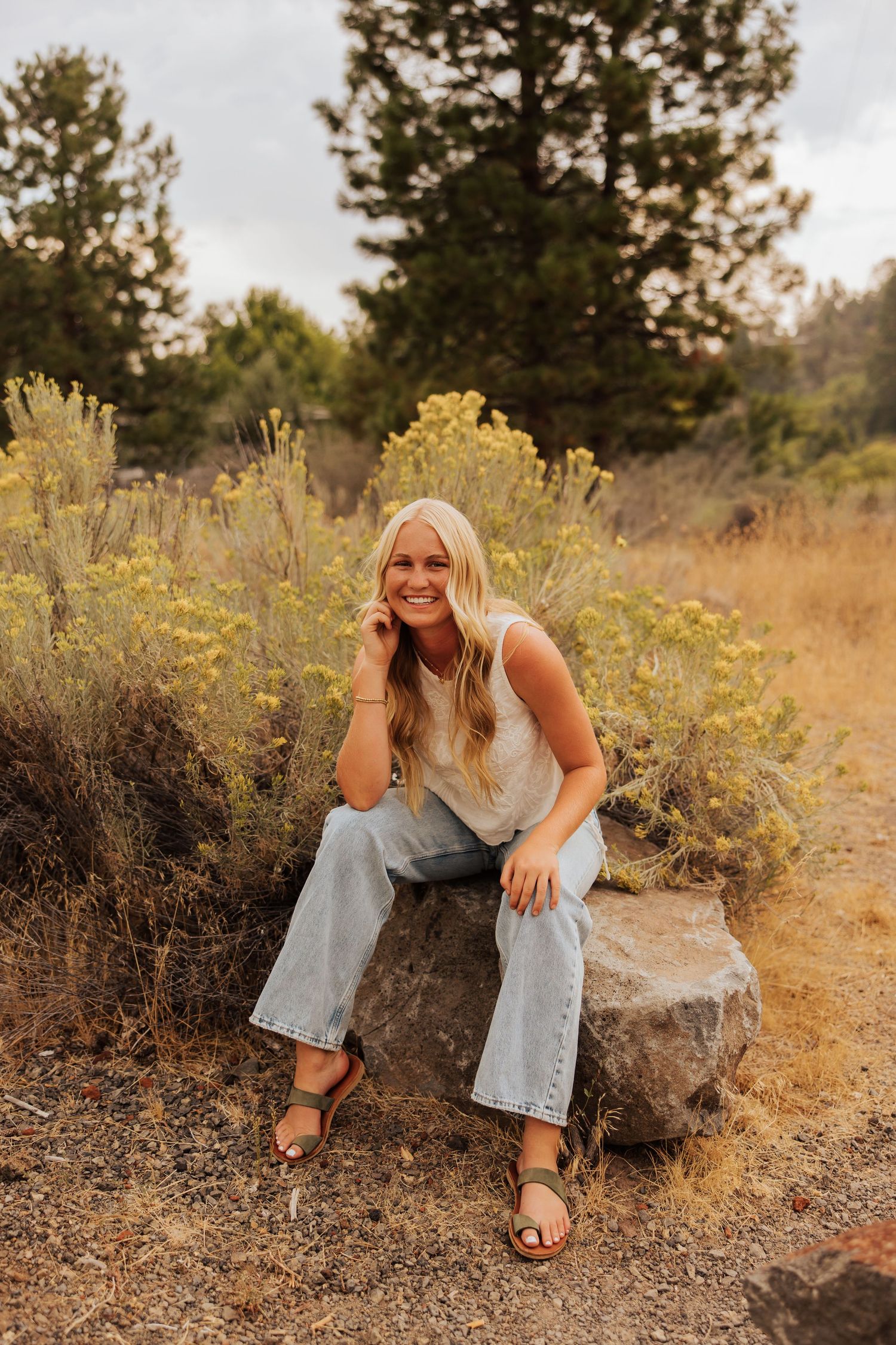 A casual outdoor photoshoot in a field with yellow wildflowers and rocks at golden hour.